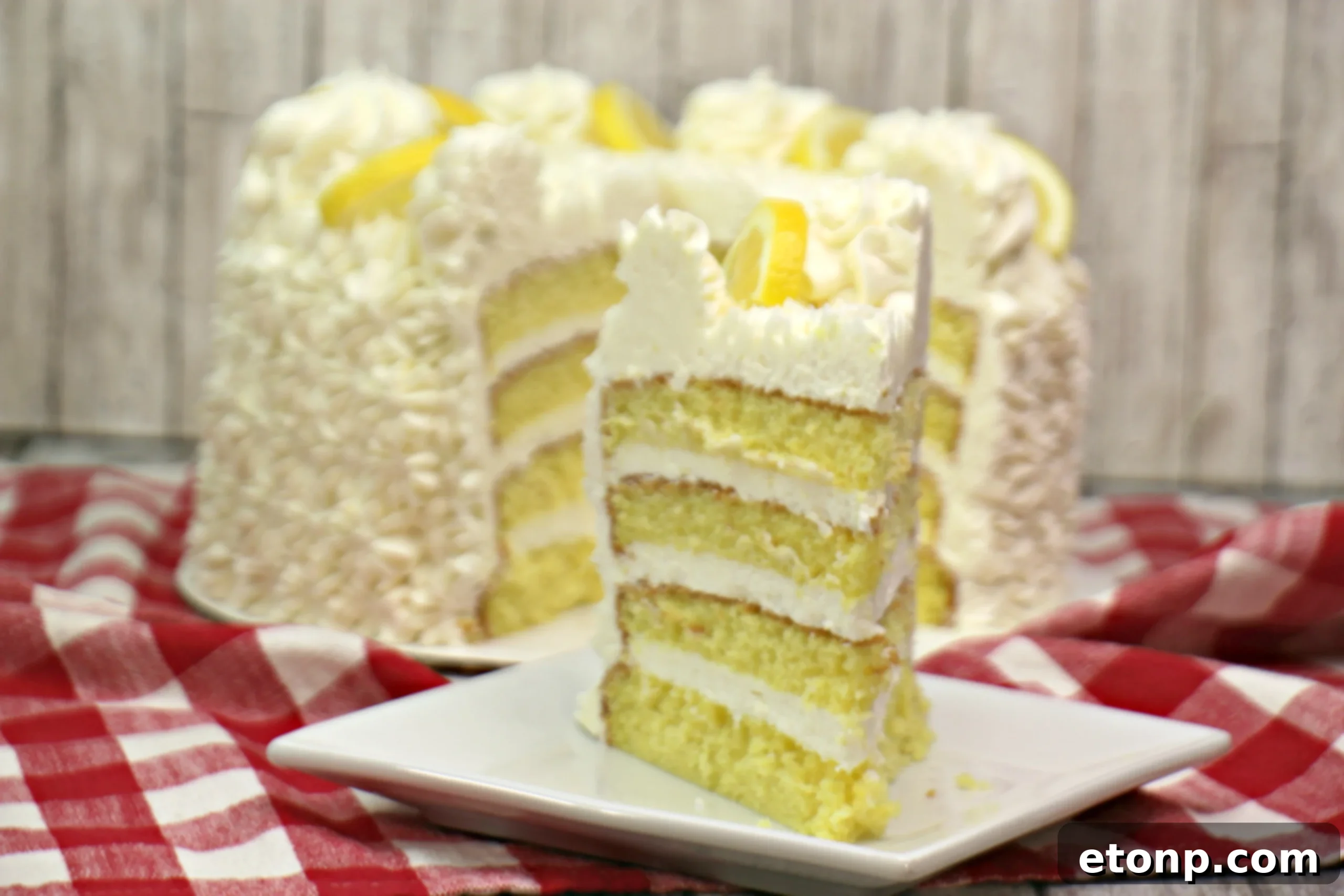 Side view of the Italian Lemon Drop Cake showing off its multiple layers and generous frosting, adorned with lemon slices.