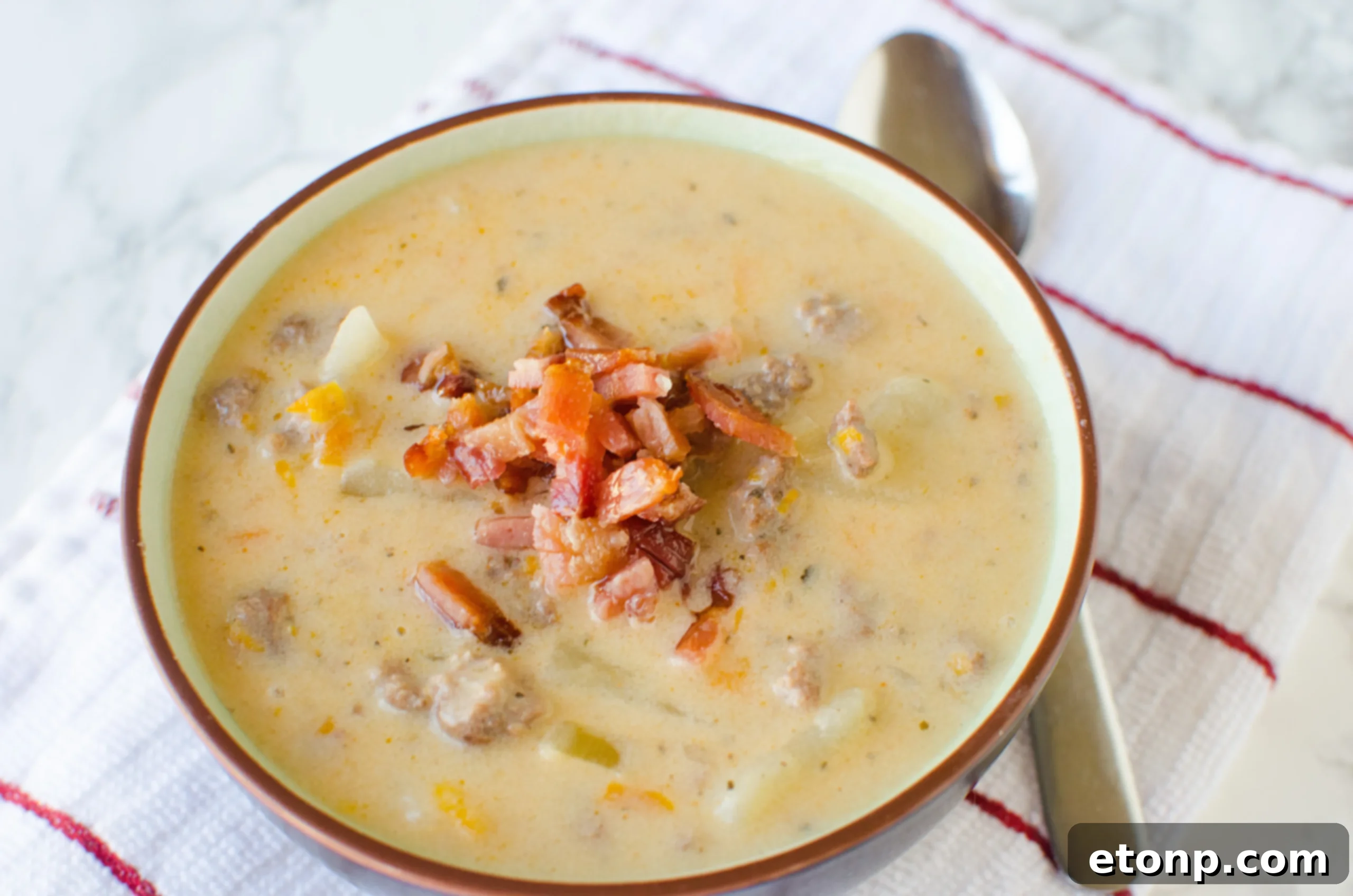 A bowl of Slow Cooker Cheeseburger Soup being stirred, showing its thick and creamy consistency.