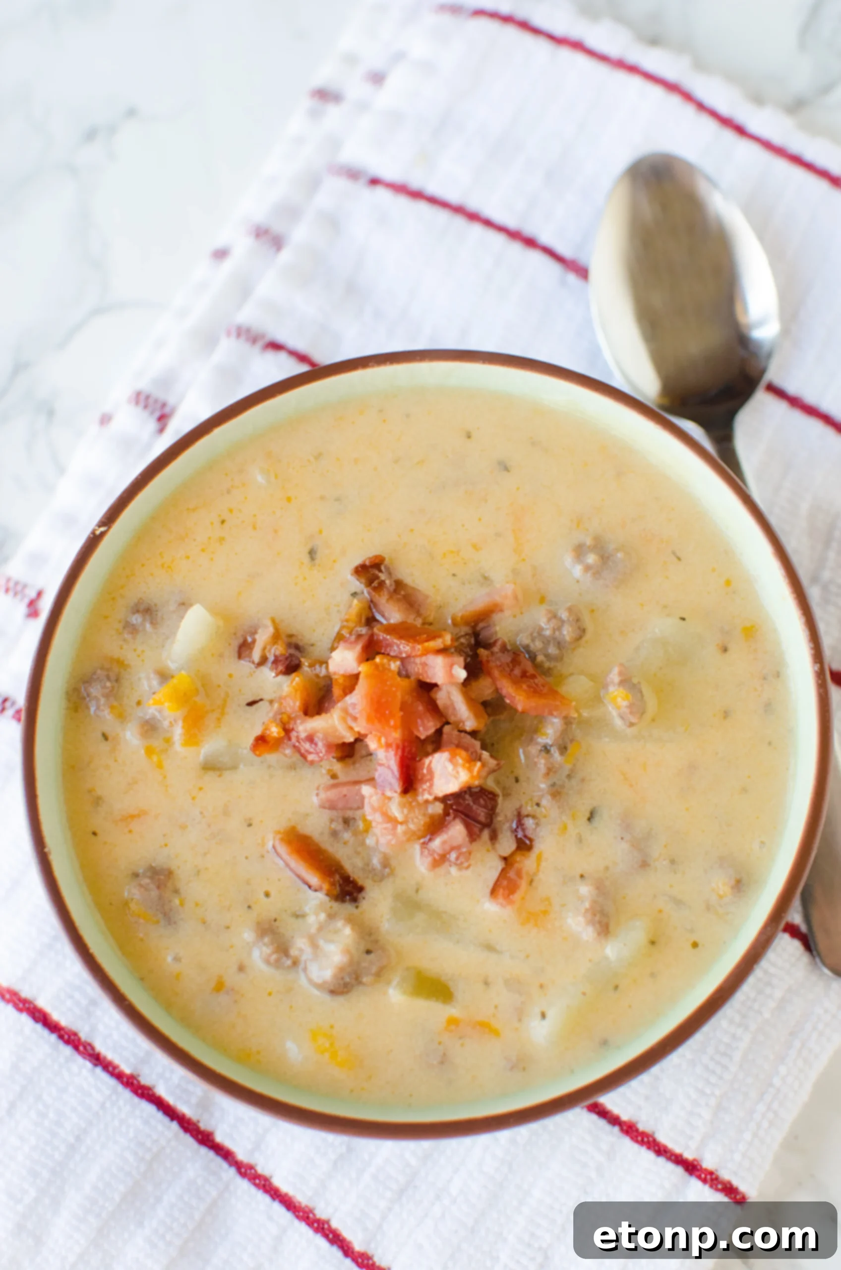 A bowl of Slow Cooker Cheeseburger Soup generously topped with crispy bacon, chopped chives, and a dollop of sour cream.