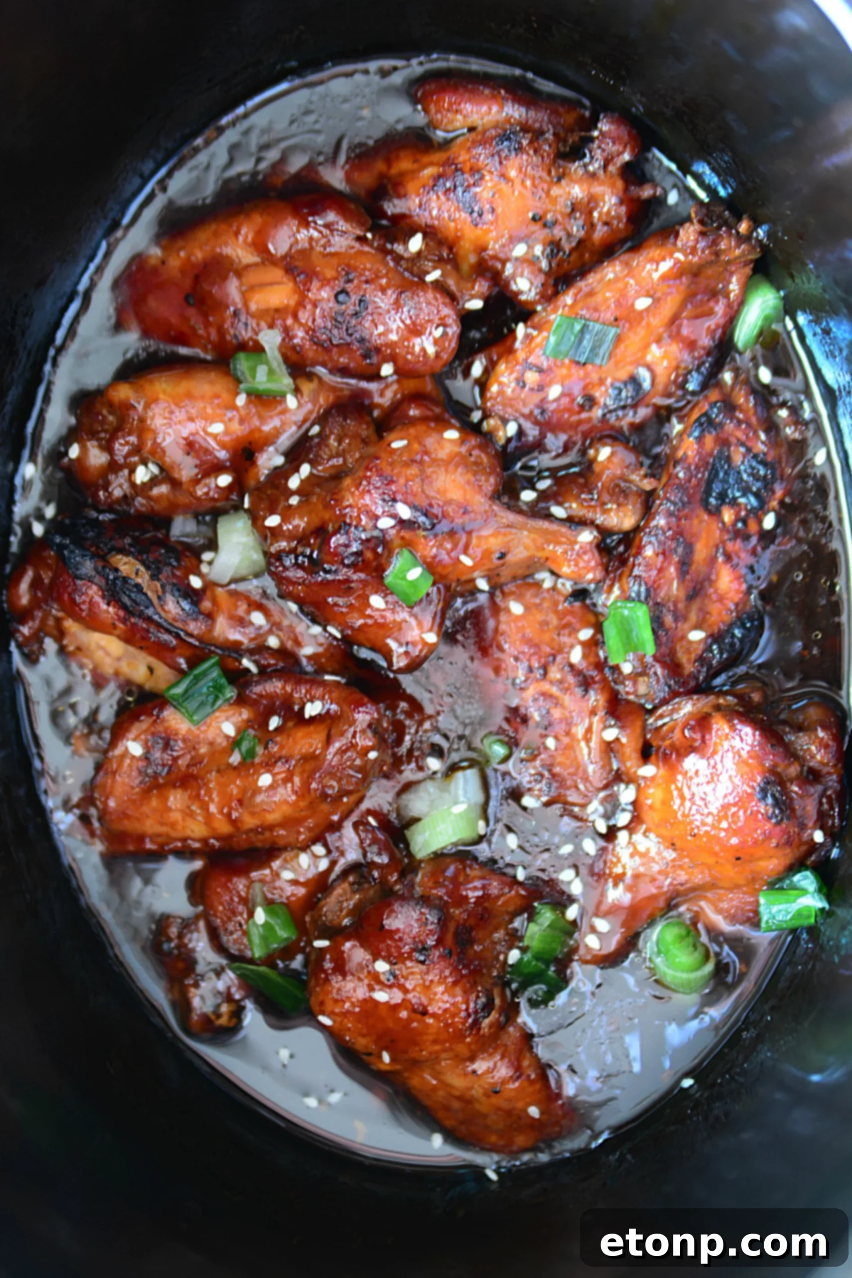 A close-up shot of crispy, glazed teriyaki chicken wings garnished with sesame seeds