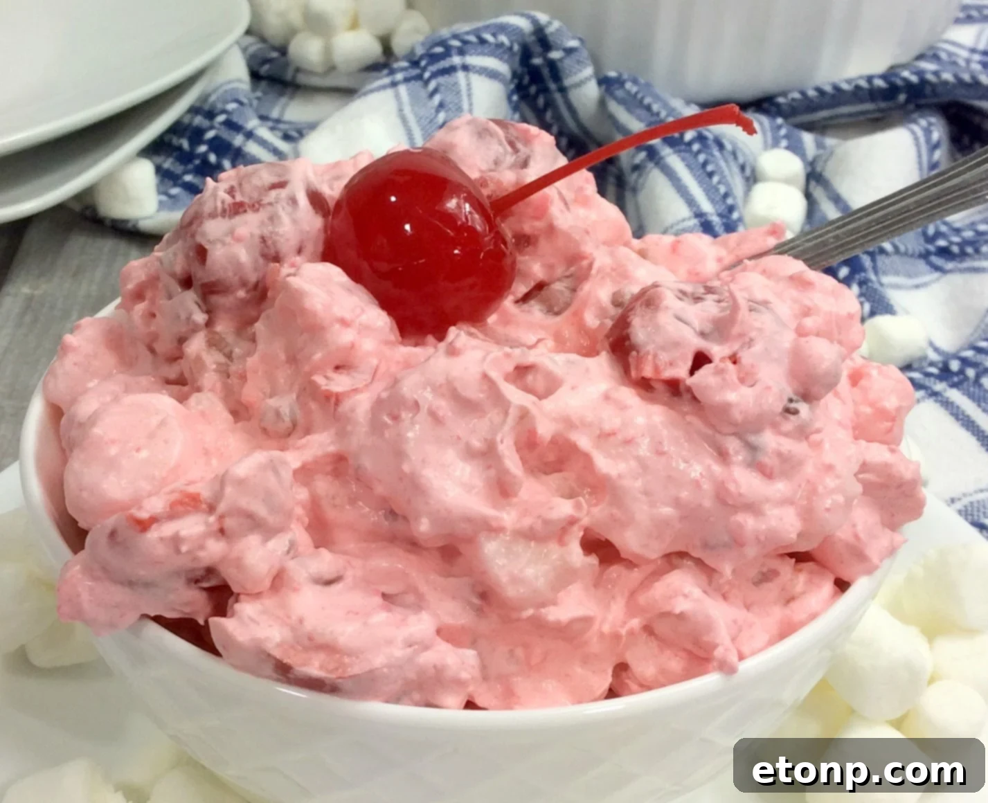 A bowl of Cherry Fluff Salad with a serving spoon, highlighting the mixture of fruit and marshmallows.