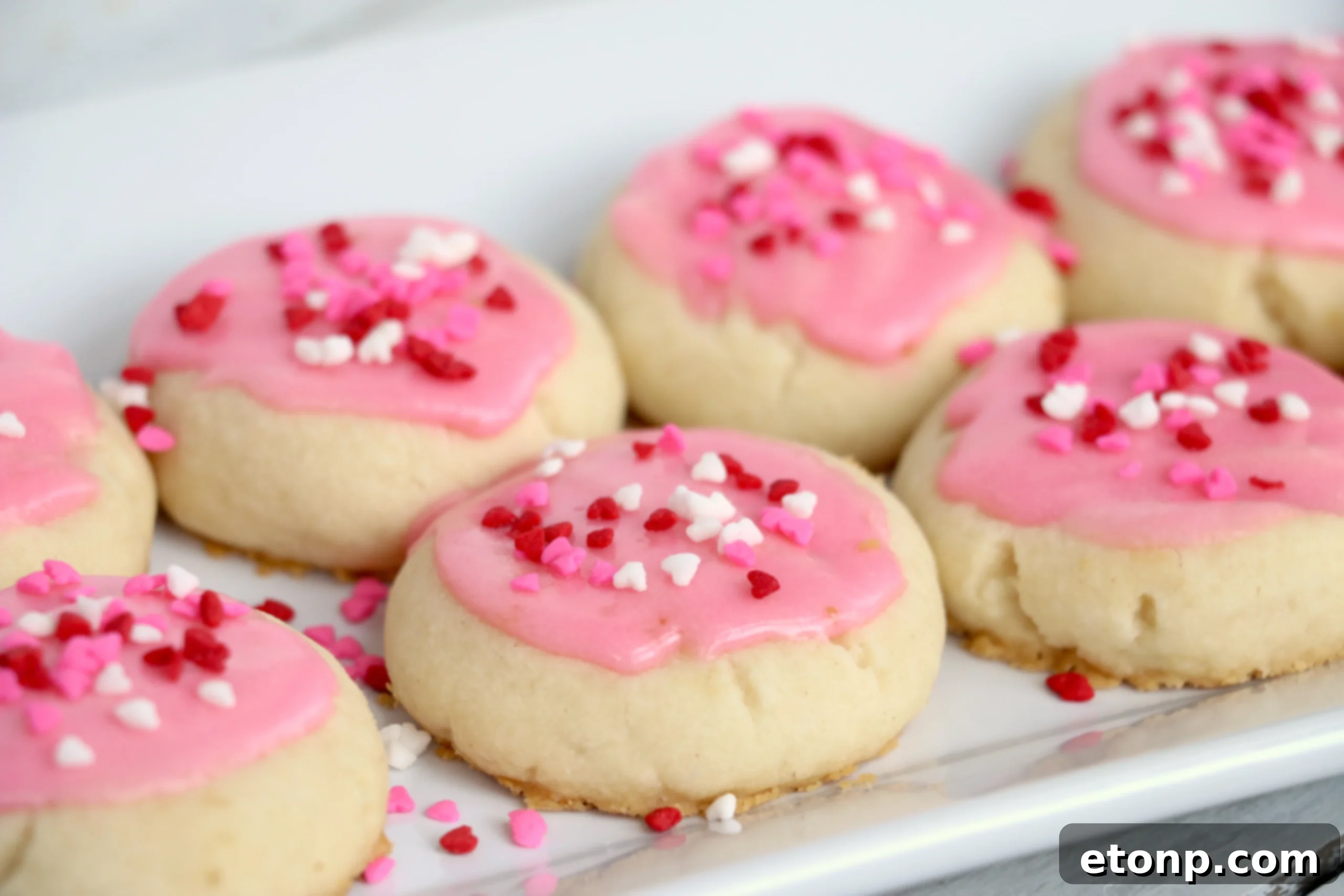 Velvet Vanilla Frosted Delights 6 Several Melt-Away Vanilla Frosted Cookies with pink icing and tiny heart sprinkles, ideal for a festive occasion.