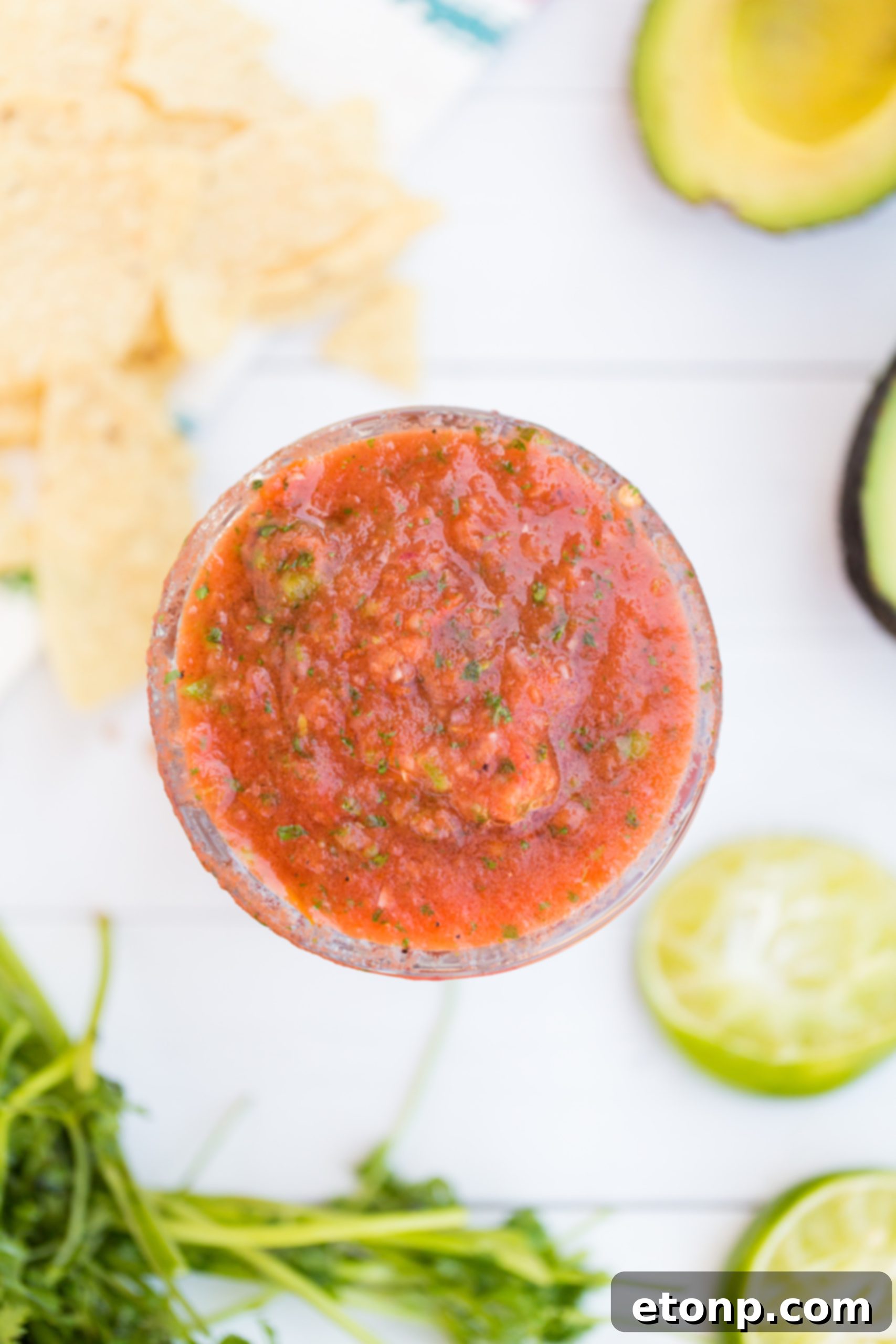 A hand carefully adding a fresh jalapeño pepper to a food processor, highlighting the customizable heat of homemade salsa.