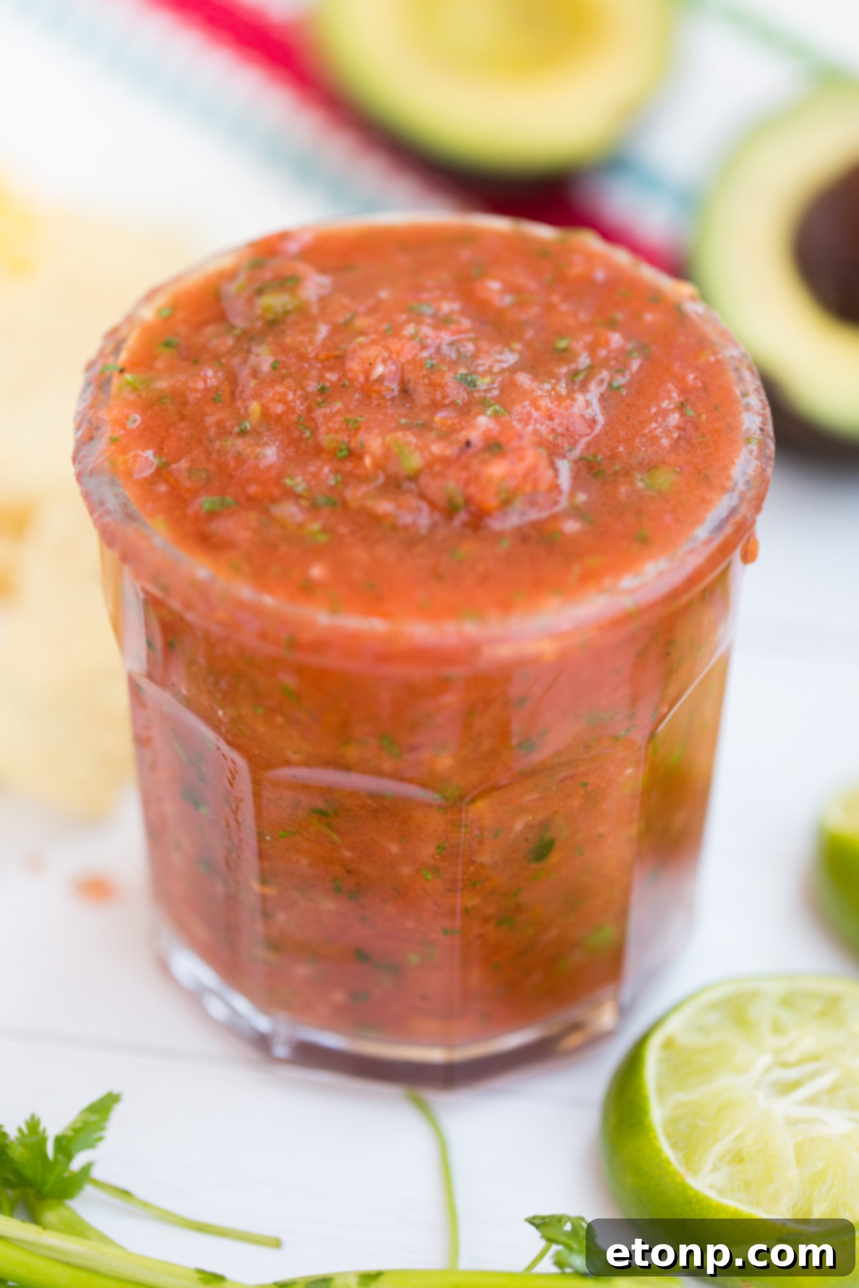 A hand gently drizzling golden honey into a bowl of prepared salsa ingredients, signifying the option to sweeten the homemade dip.