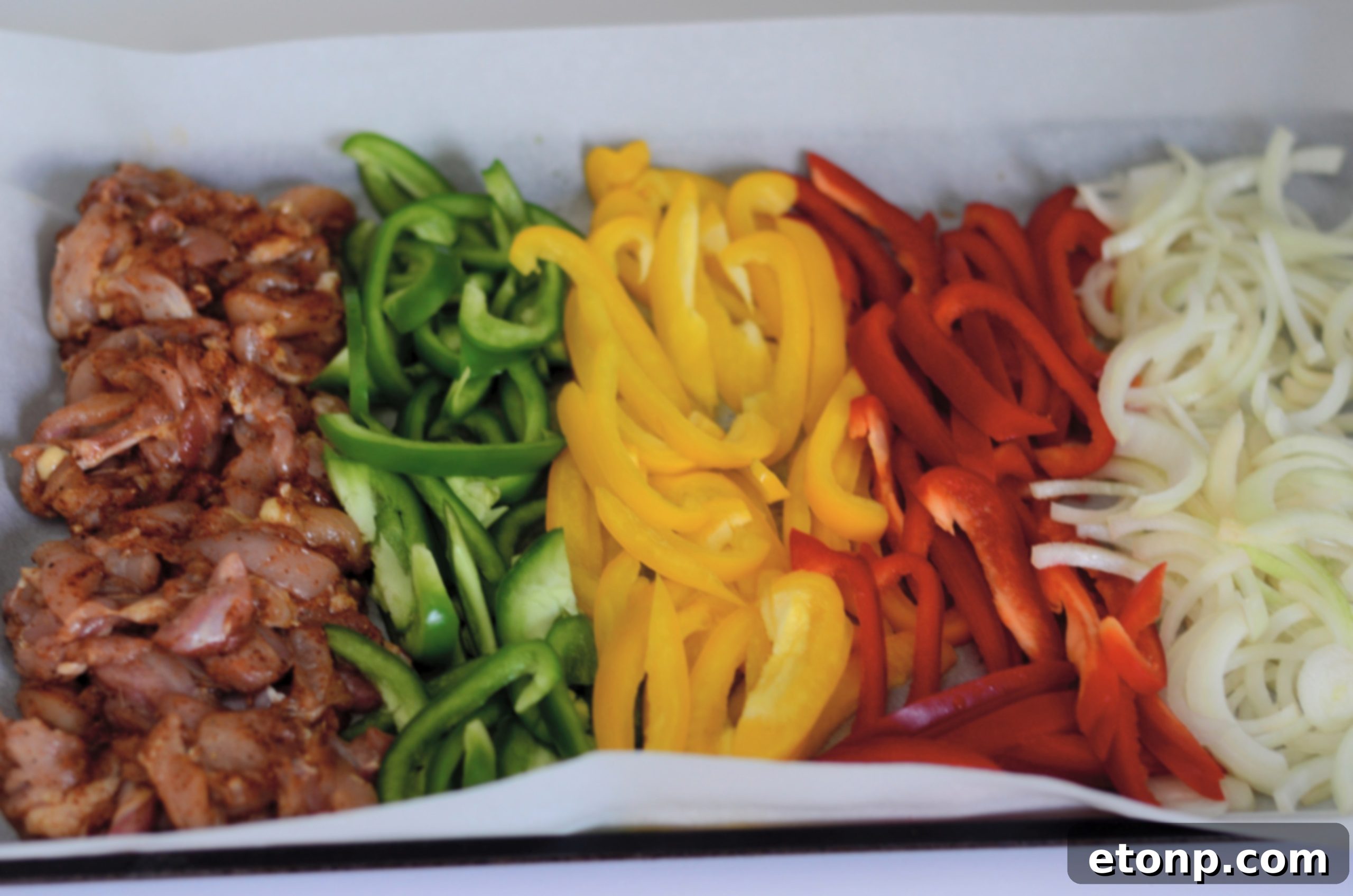 Raw chicken strips, red, green, and yellow bell peppers, and sliced yellow onion arranged on a baking sheet, ready for seasoning and cooking.