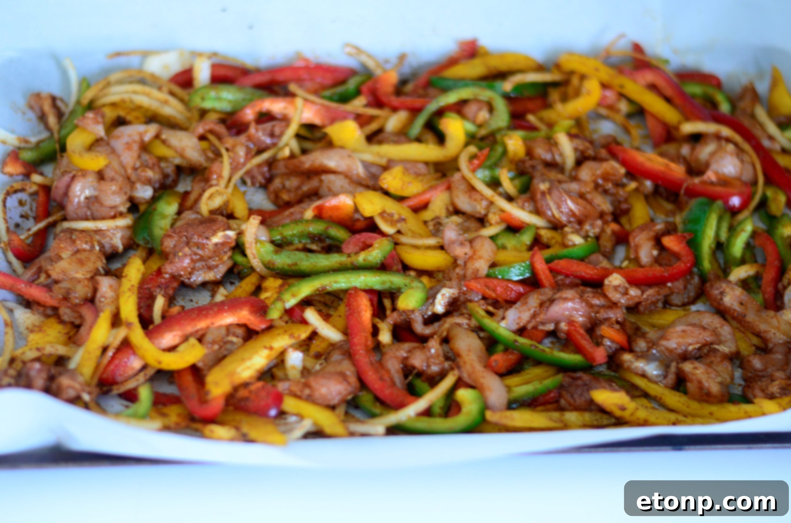 Another view of raw chicken fajita ingredients on a sheet pan, showcasing thinly sliced bell peppers and onions before cooking.