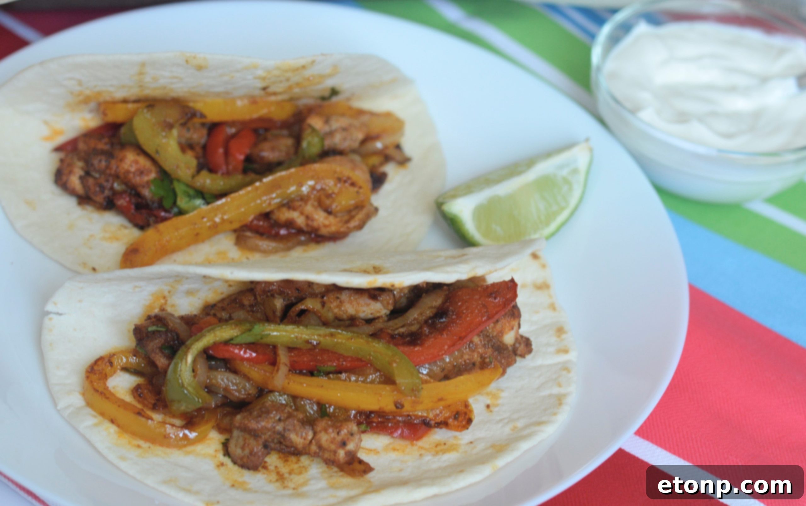 An appetizing spread of sheet pan chicken fajitas, warm tortillas, and various toppings including sour cream, salsa, and lime slices.