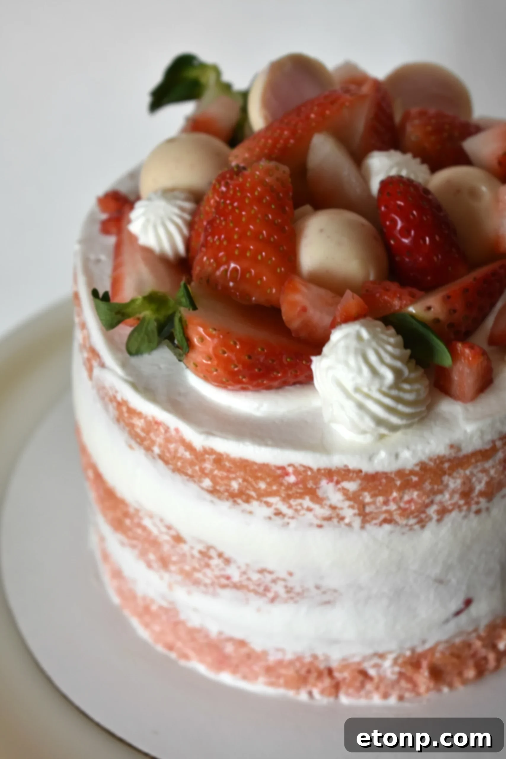 A beautifully decorated Strawberry Creamsicle Layered Cake, showcasing its vibrant pink layers and fluffy white frosting, topped with fresh strawberries.