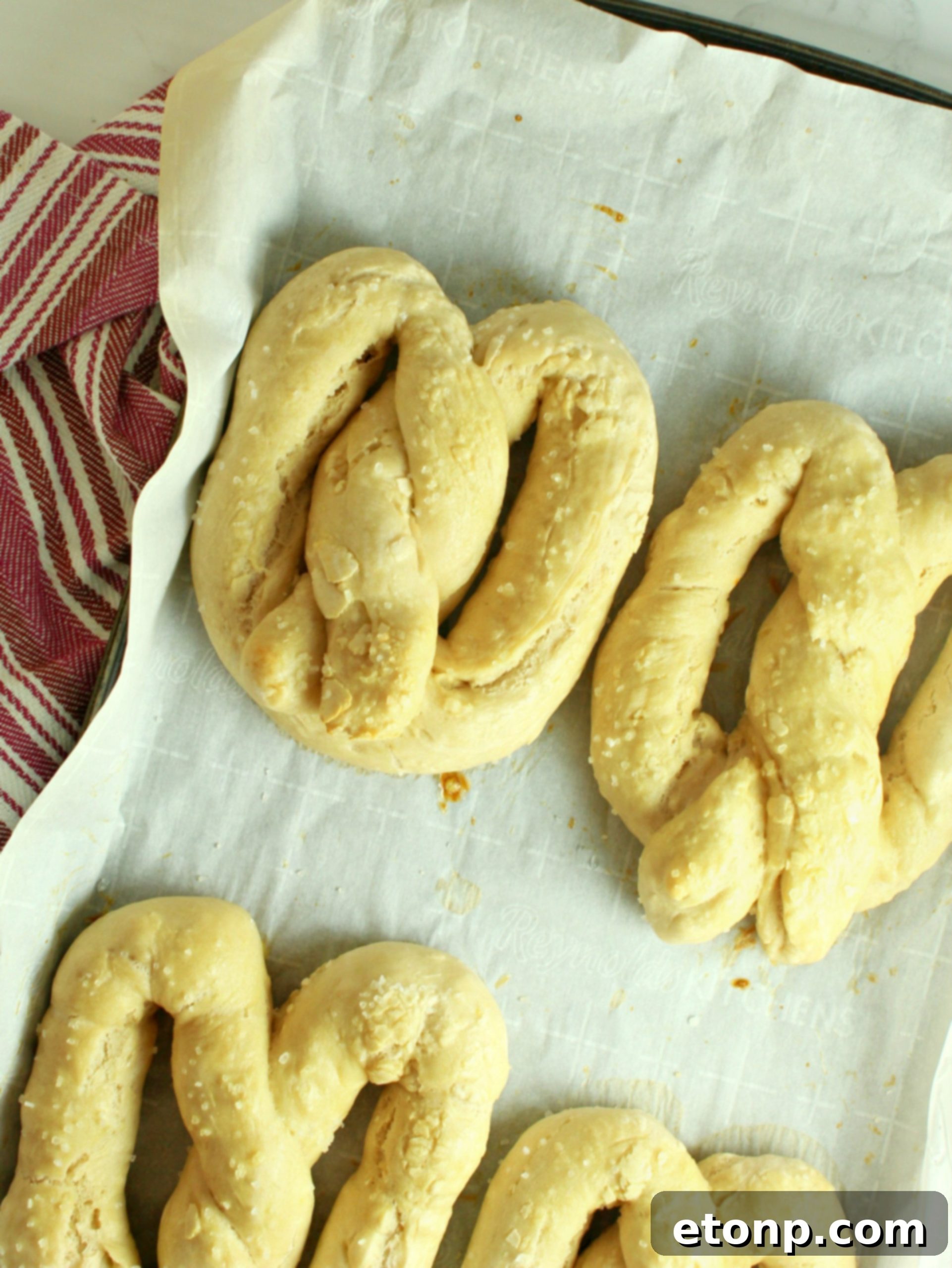 Hand-shaped soft pretzels on a baking sheet, brushed with egg wash and ready for the oven.