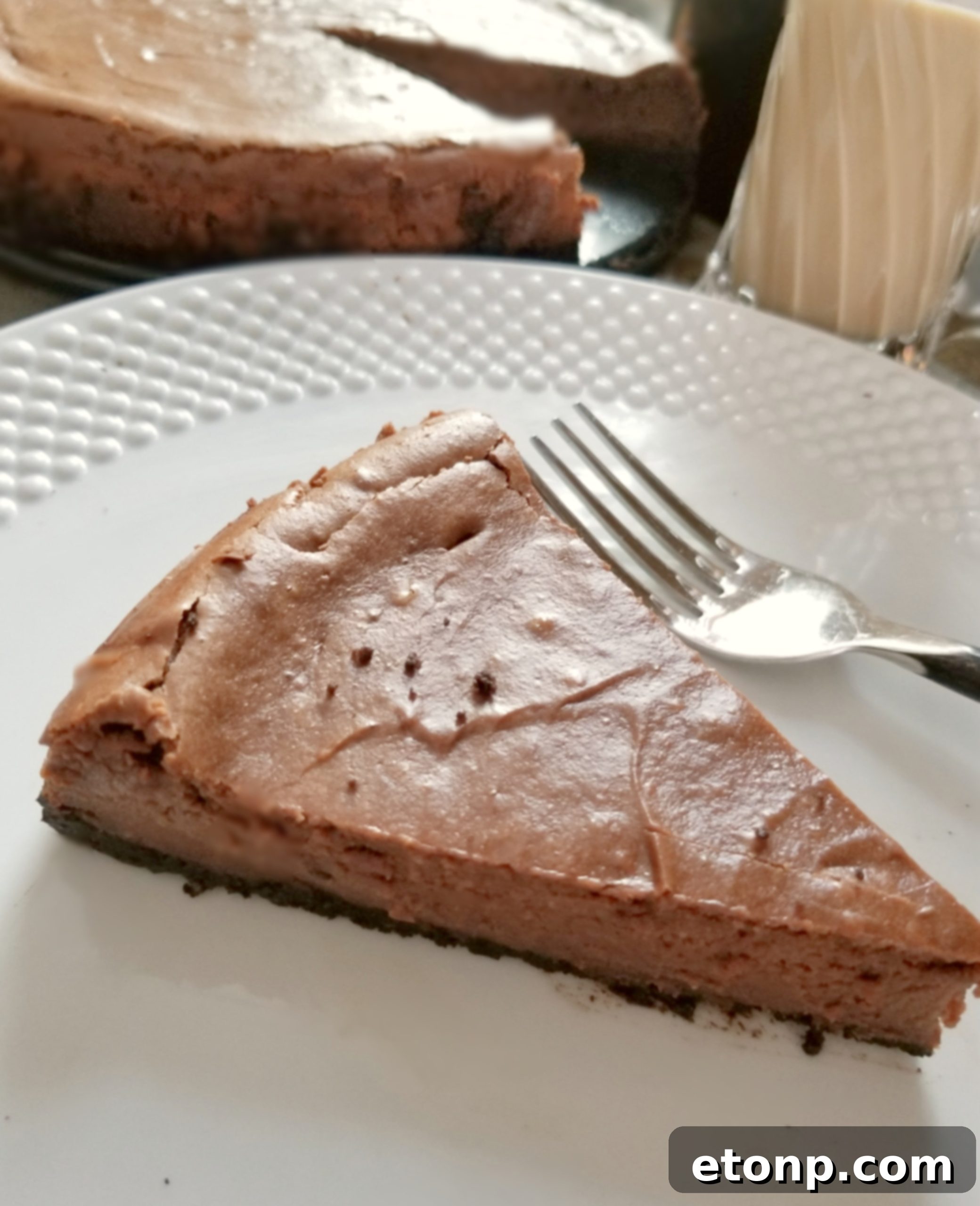 A slice of Bailey's Chocolate Cheesecake on a plate, showing the layers of crust and filling.