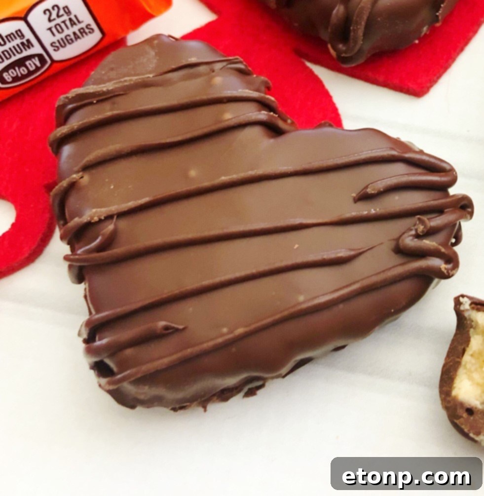 A top-down view of several heart-shaped peanut butter fillings, some coated in chocolate and some waiting to be dipped, on a baking sheet with parchment paper.