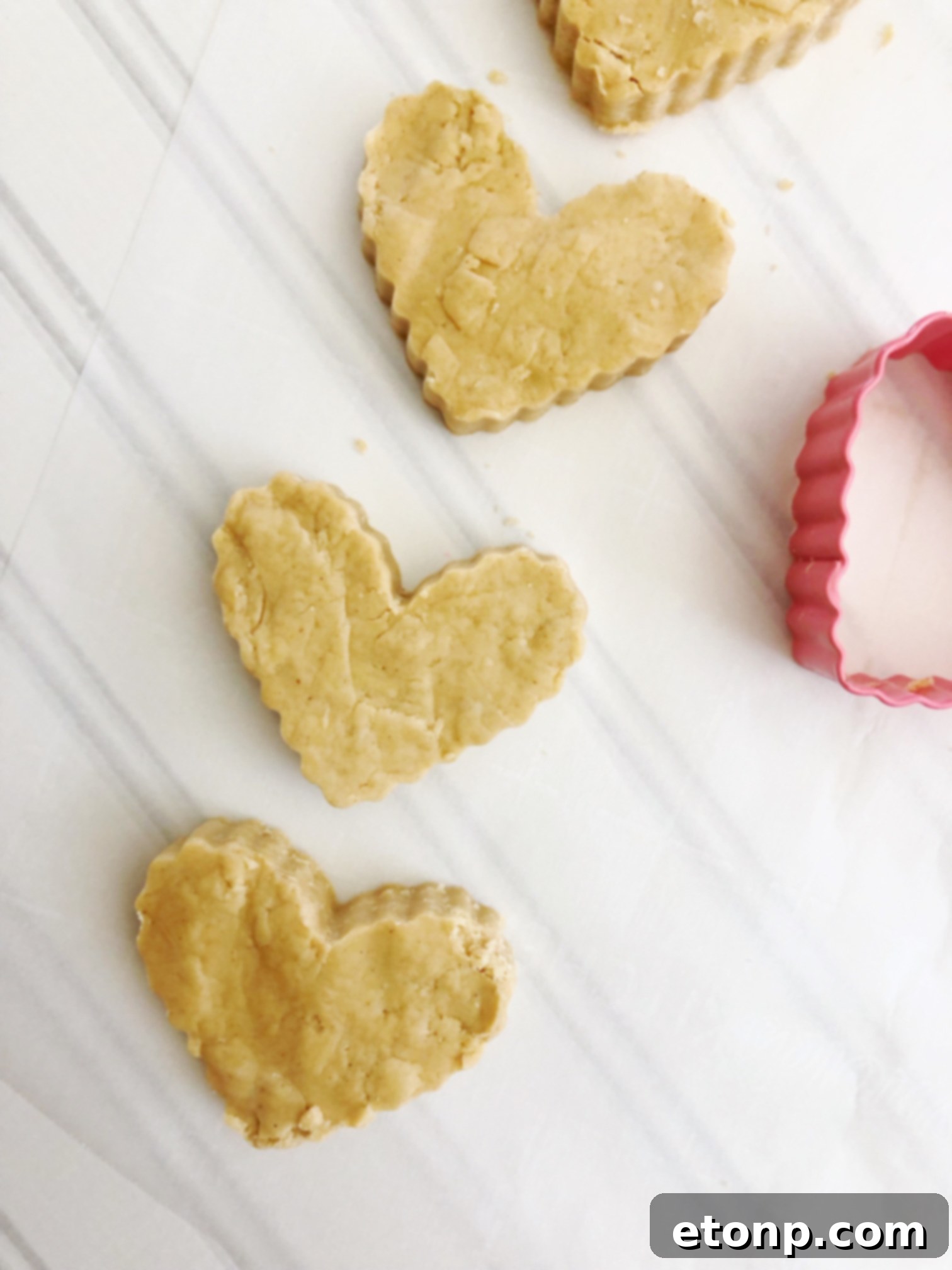 A hand holding a freshly dipped Reese's Peanut Butter Heart, with melted chocolate dripping slightly, highlighting the glossy finish.
