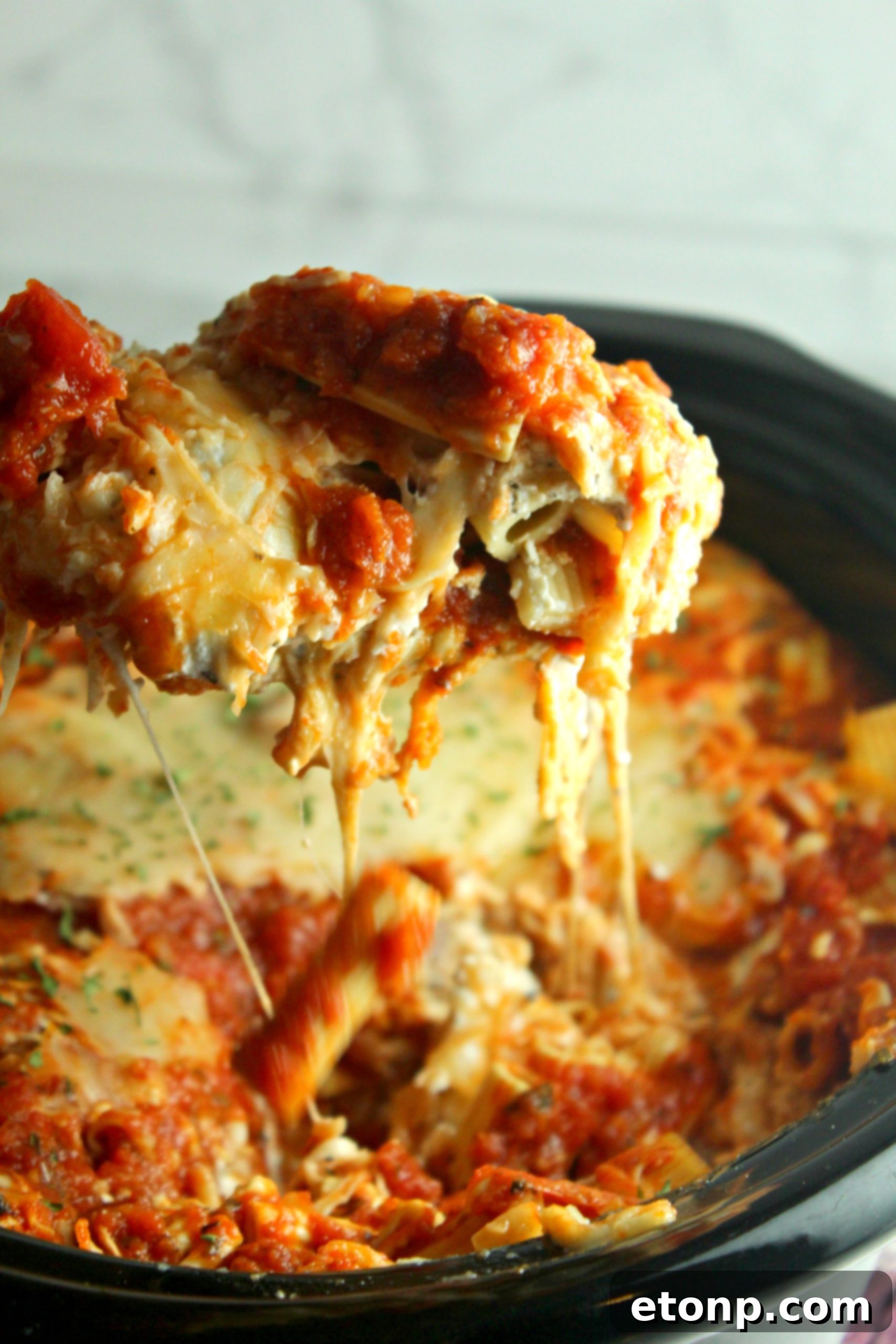 Set It and Forget It Cheesy Baked Ziti 10 Close-up of a serving of baked ziti with visible layers of pasta, sauce, meat, and melted cheese, garnished with fresh basil.