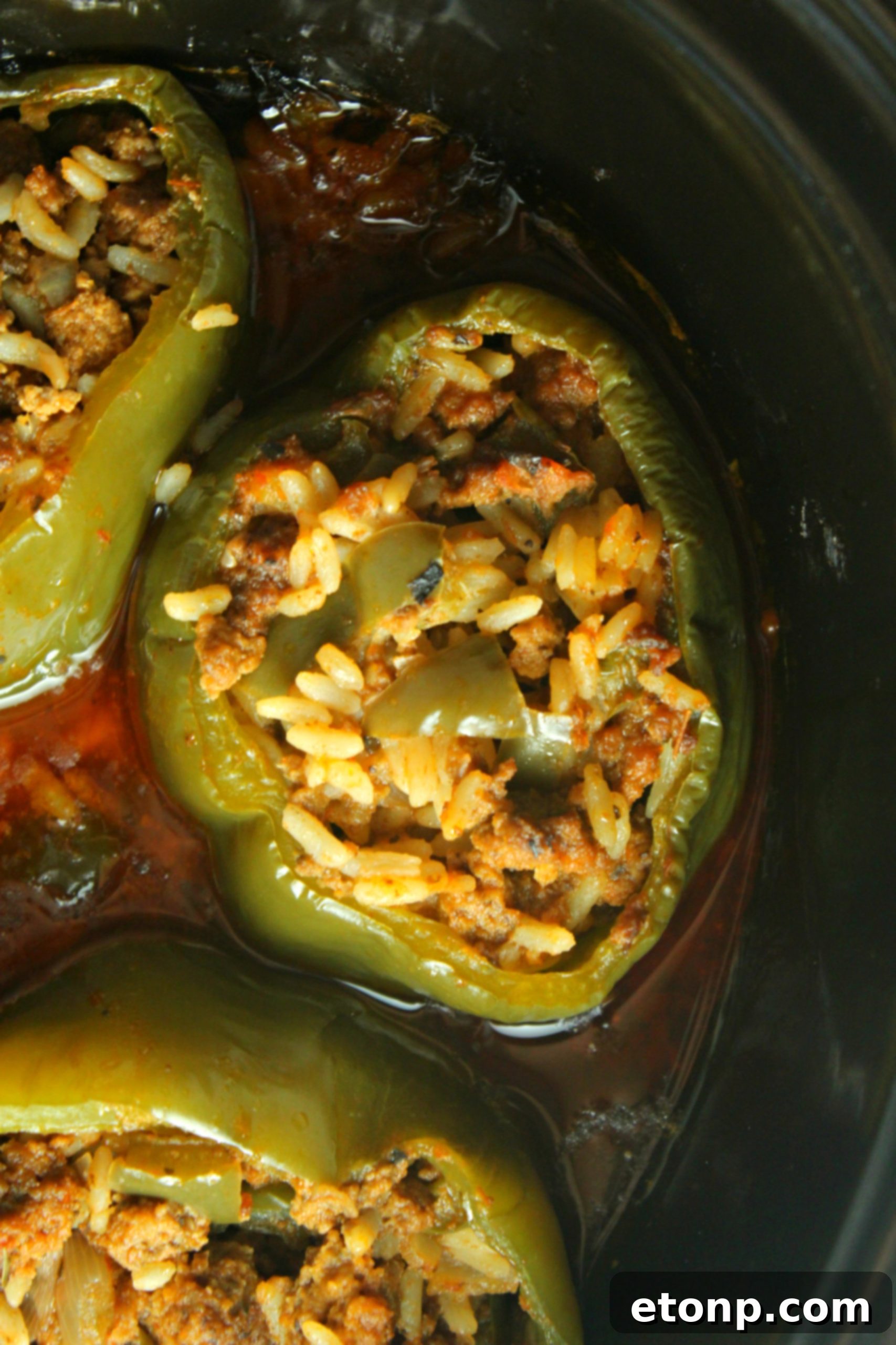 Effortless Slow Cooker Stuffed Peppers 4 A close-up of a slow cooker filled with vibrant green stuffed bell peppers, simmering in a rich red sauce, ready to be cooked.
