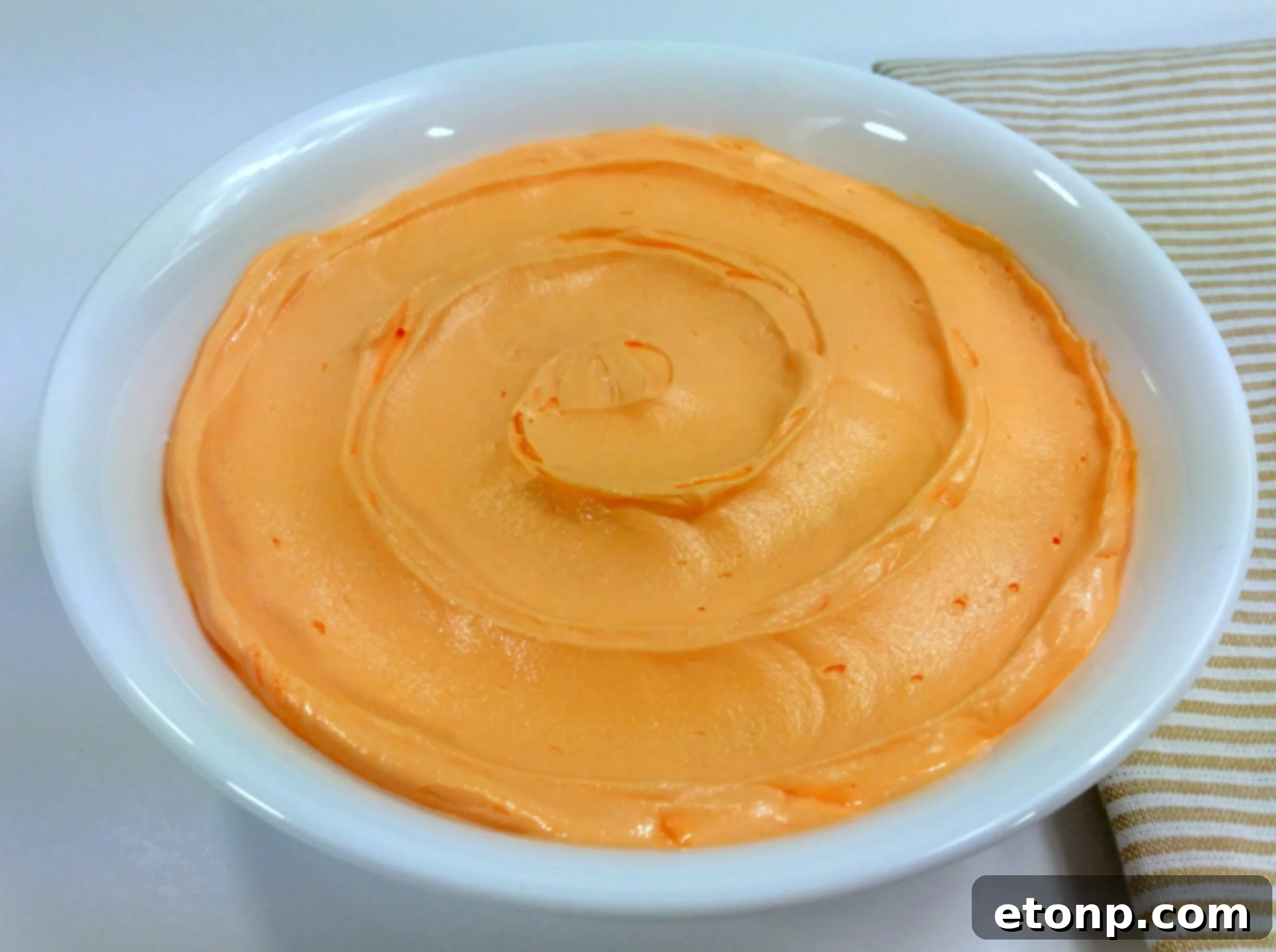 Close-up shot of perfectly smooth and fluffy orange buttercream frosting, ready for piping.