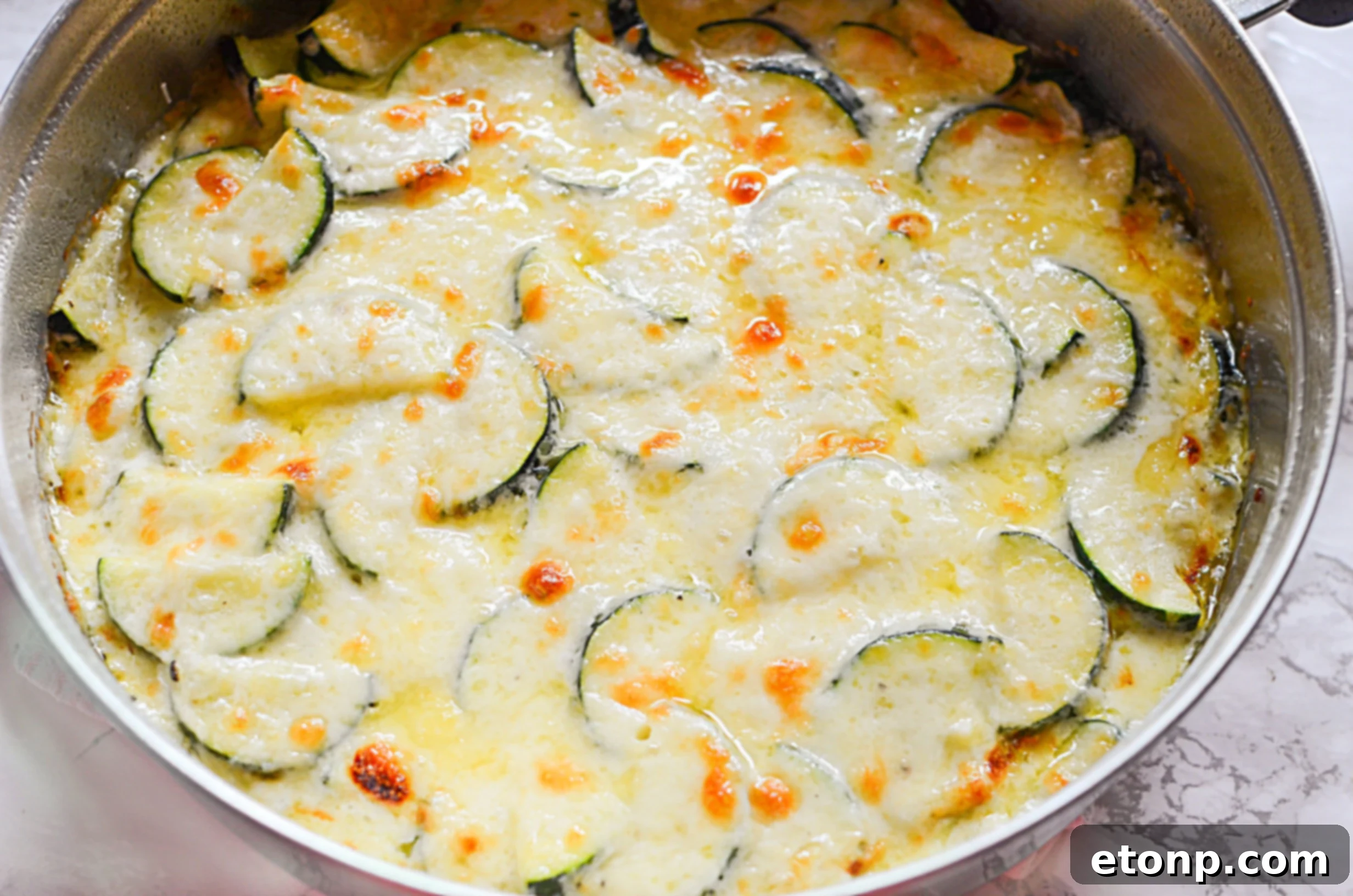 Close-up of golden brown cheesy zucchini gratin, fresh out of the oven, with a creamy texture visible, garnished with fresh herbs.