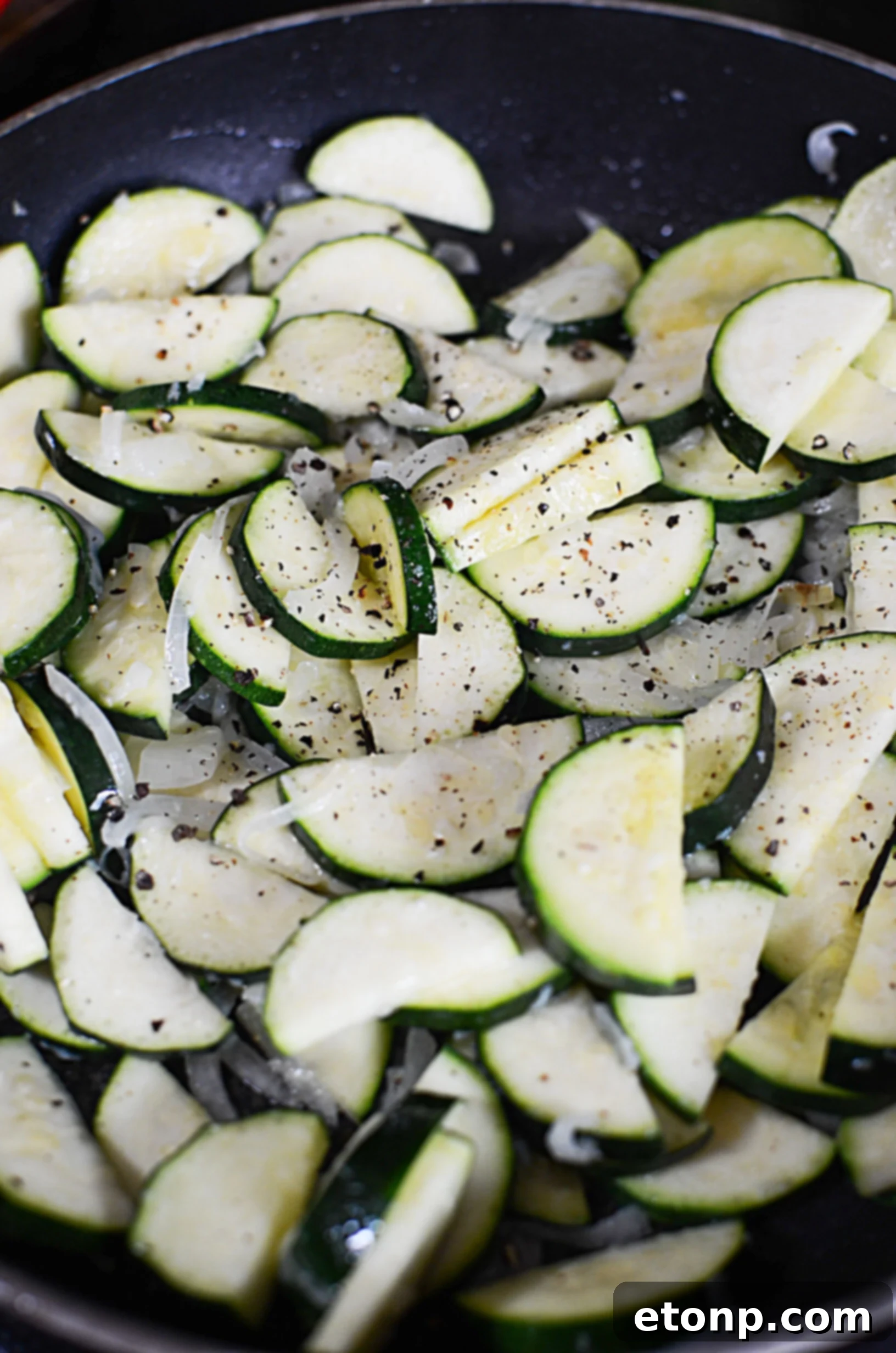 Overhead shot of a skillet filled with cheesy zucchini gratin, garnished with fresh herbs, steam rising, ready to be served.