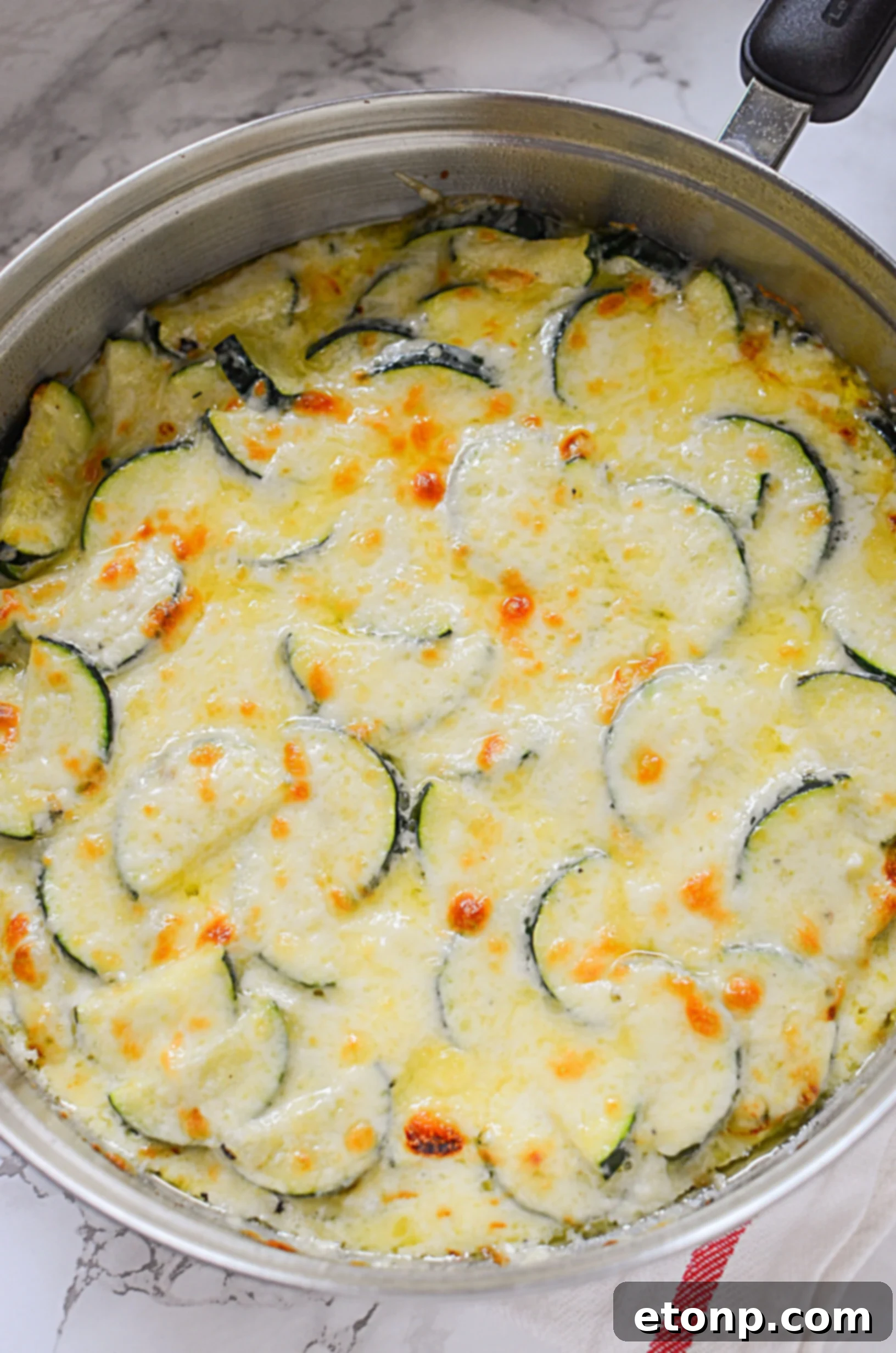 A close-up side view of cheesy zucchini gratin in a rustic baking dish, showcasing the layers of tender zucchini and beautifully melted, bubbly cheese.