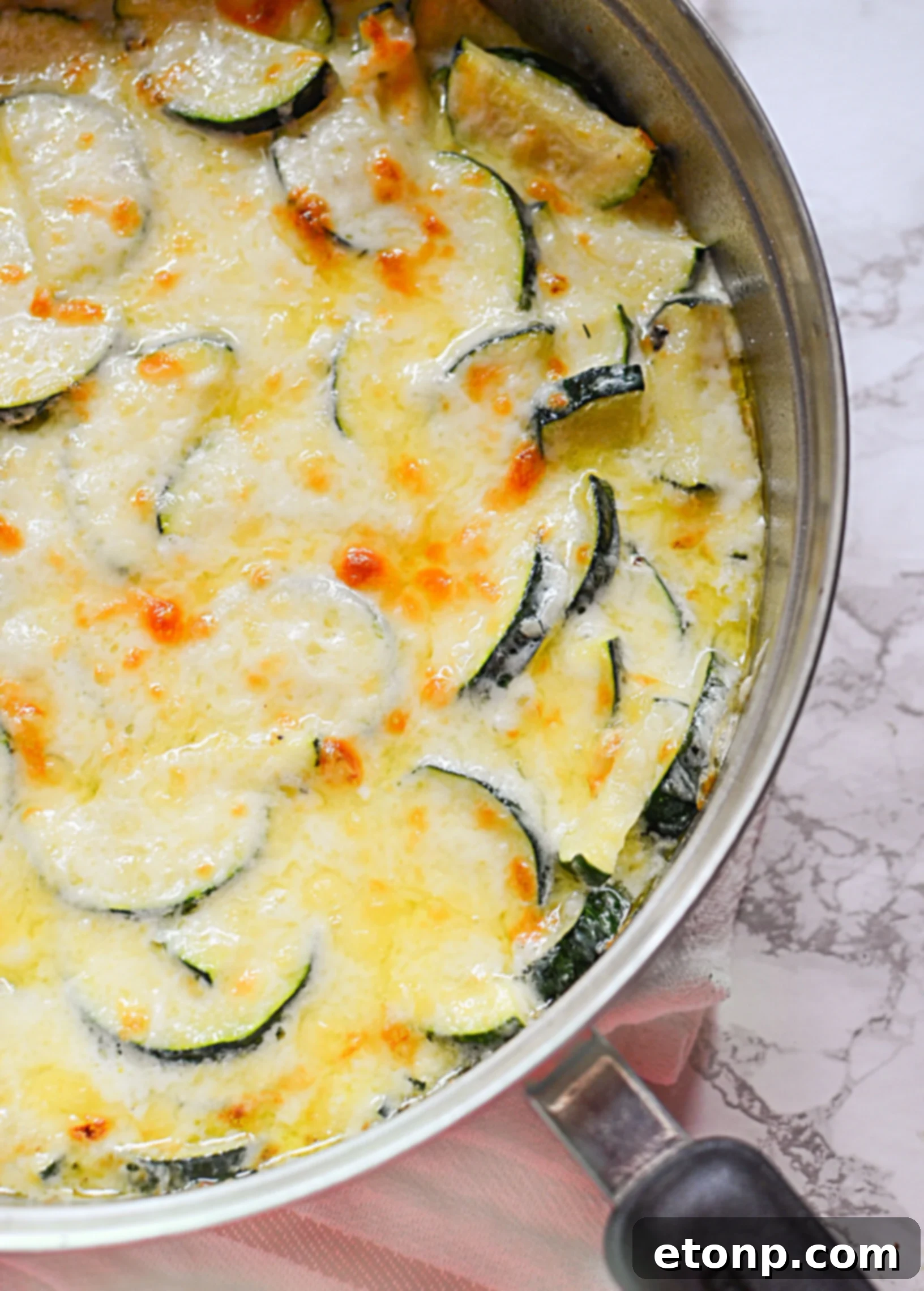 Serving spoon lifting a generous portion of creamy, cheesy zucchini gratin from the skillet, clearly showing the tender zucchini slices enveloped in sauce.