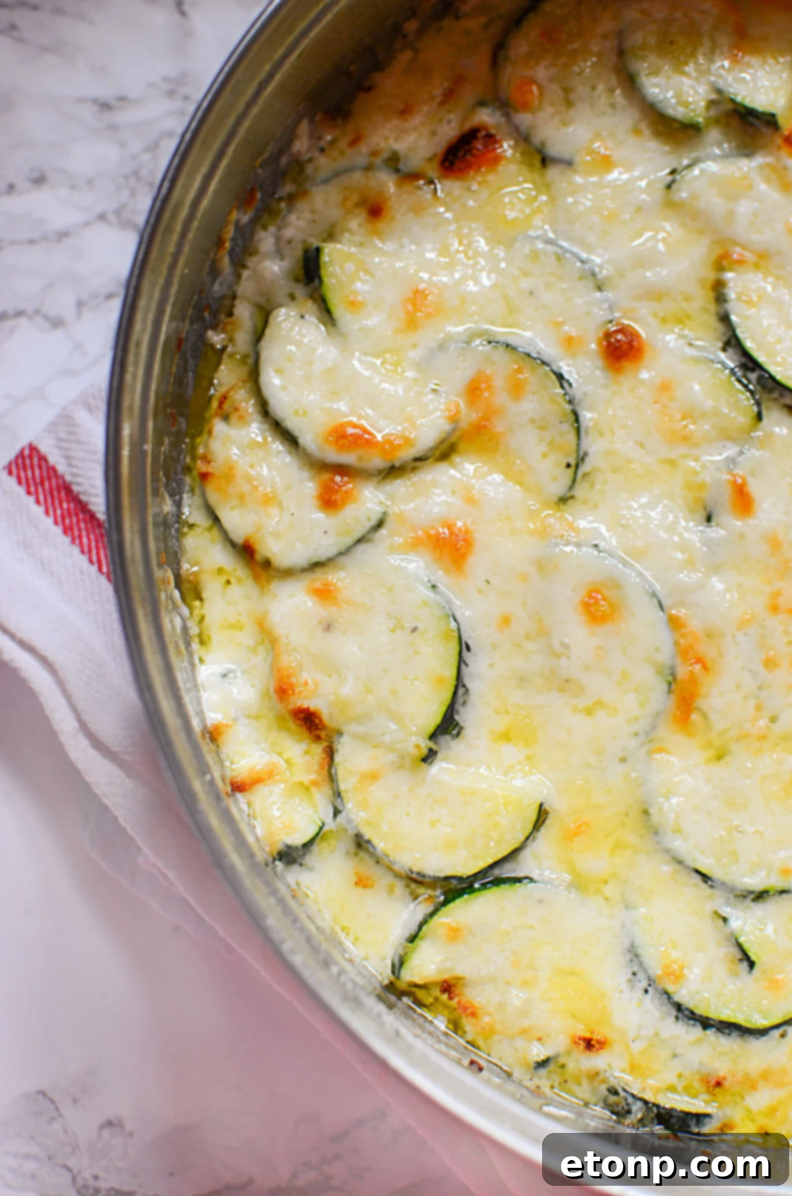 A different angle of the cooked zucchini gratin in the skillet, showing the golden-brown, crispy edges and the enticing bubbly cheese topping.