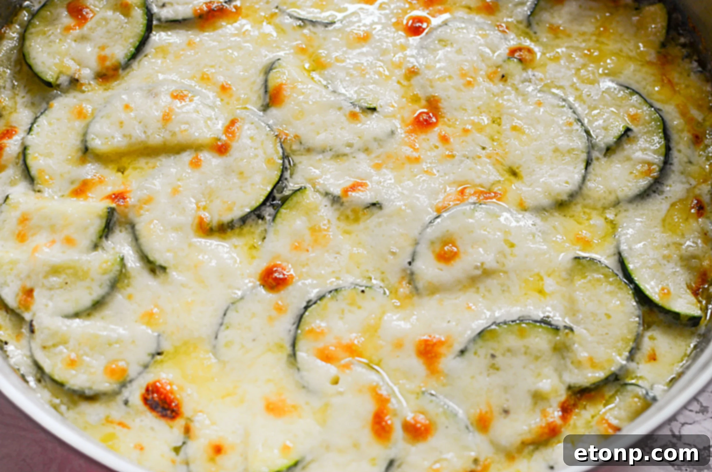 Raw ingredients for zucchini gratin: thinly sliced zucchini, various cheeses, whole and minced fresh garlic, and an onion.