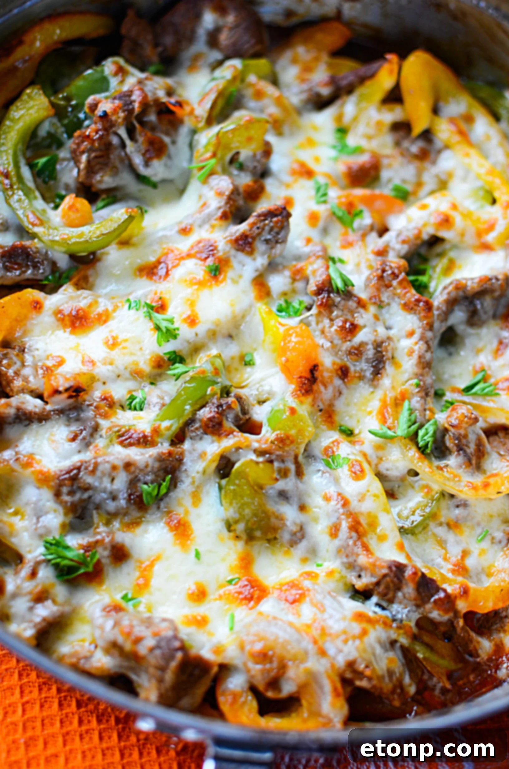 The melted cheese cascading over the steak and vegetables in the skillet, creating a rich, appetizing texture.