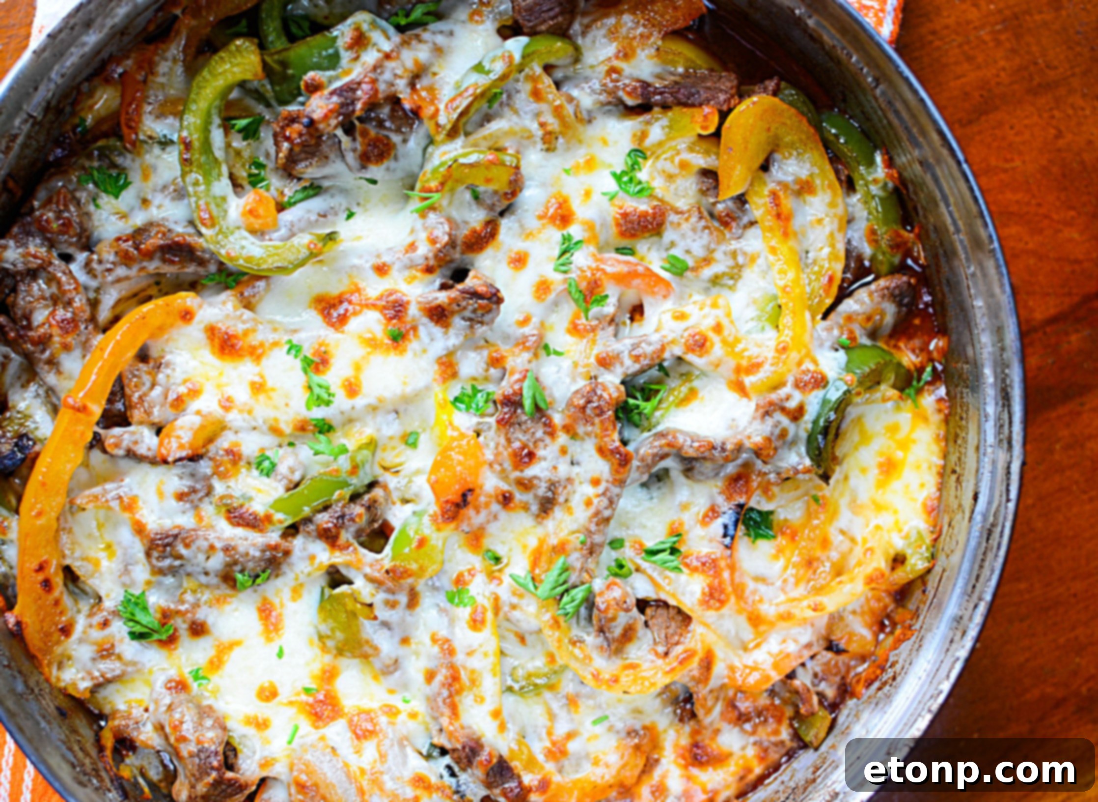 A close-up of the gooey melted cheese on top of the cooked steak, onions, and peppers in the skillet.