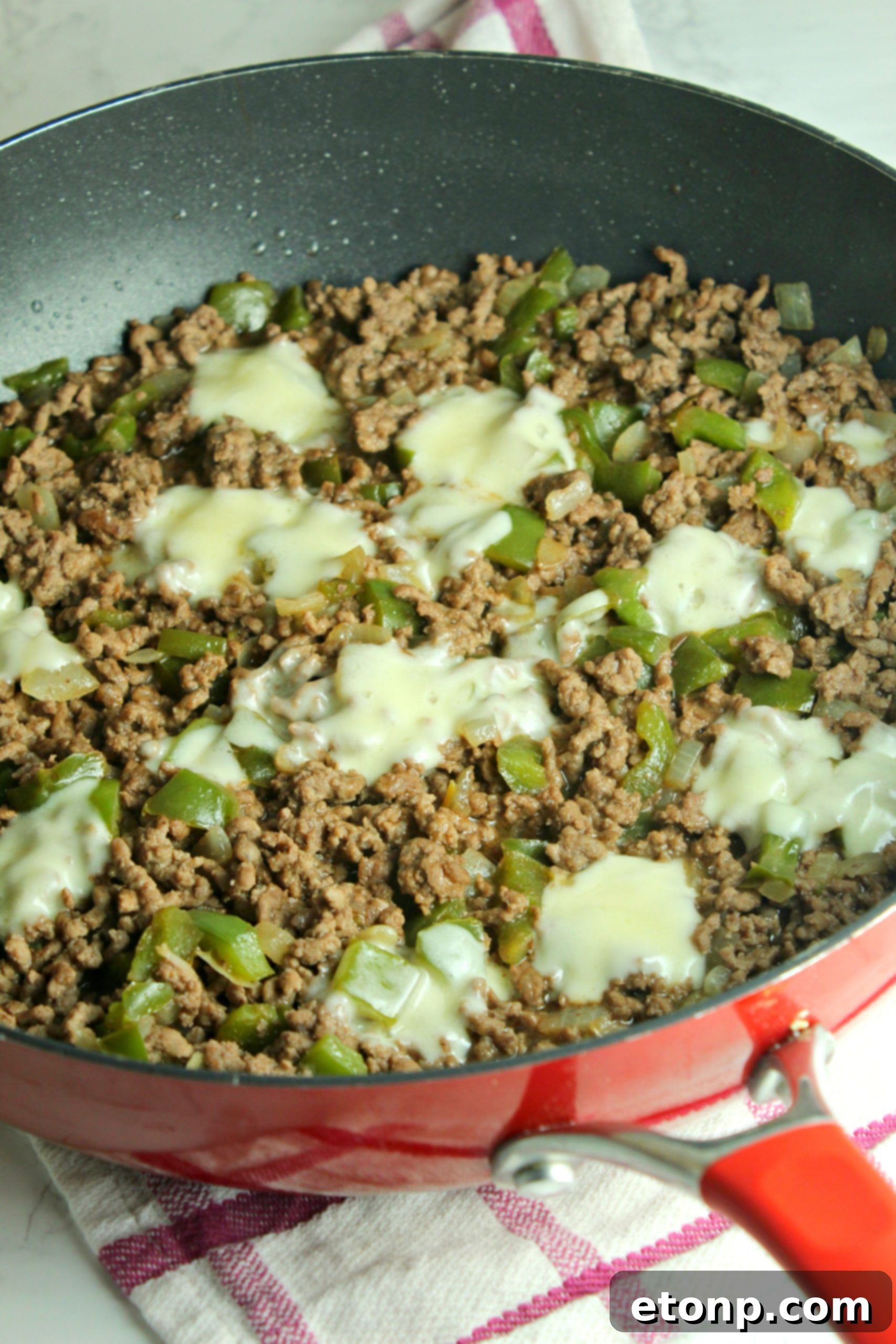 Close-up of a single Cheesesteak Sloppy Joe, showing the beef, peppers, and melted cheese spilling out.