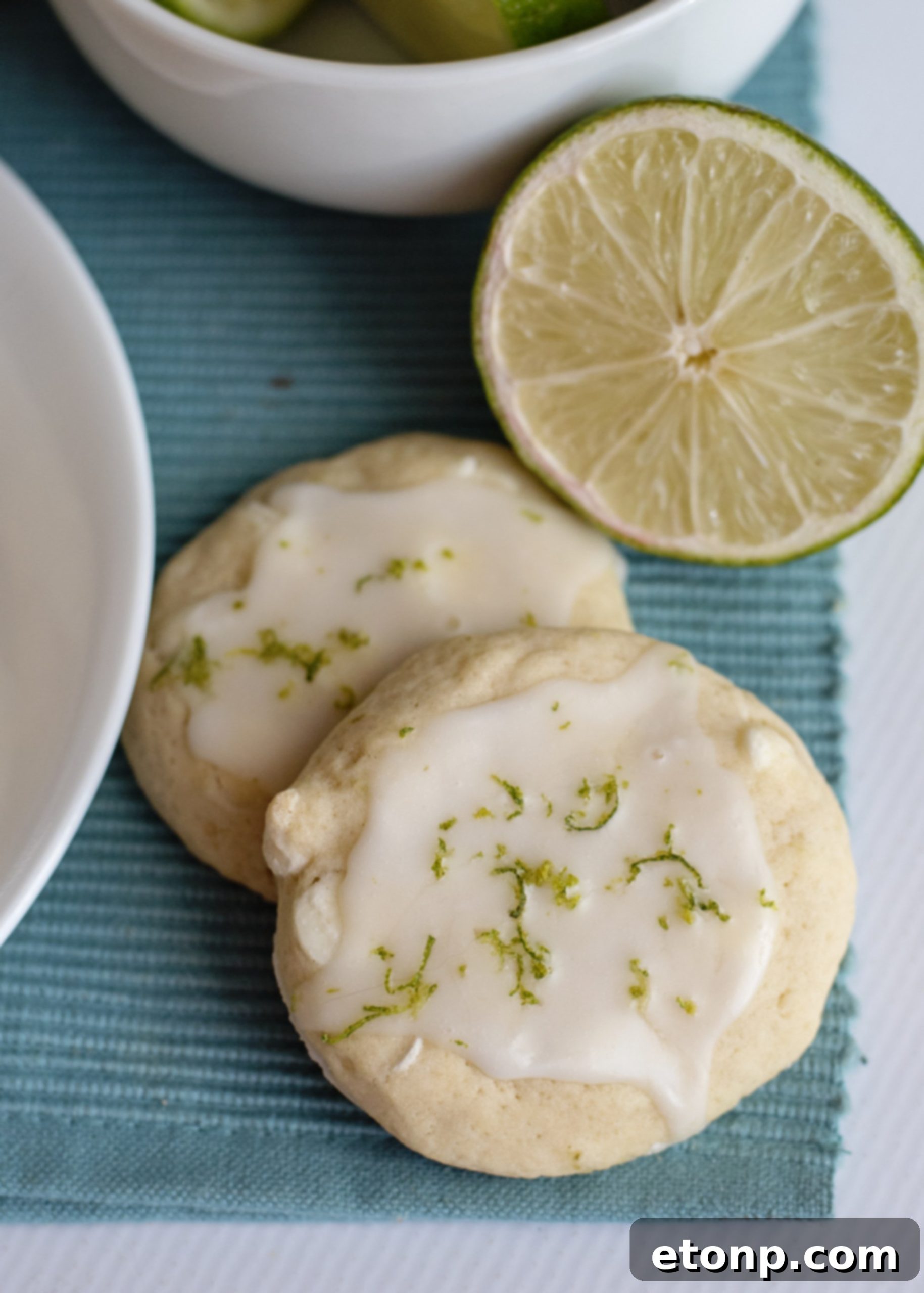 Freshly baked Key Lime Pie Cookies cooling on a wire rack with whole limes in the background