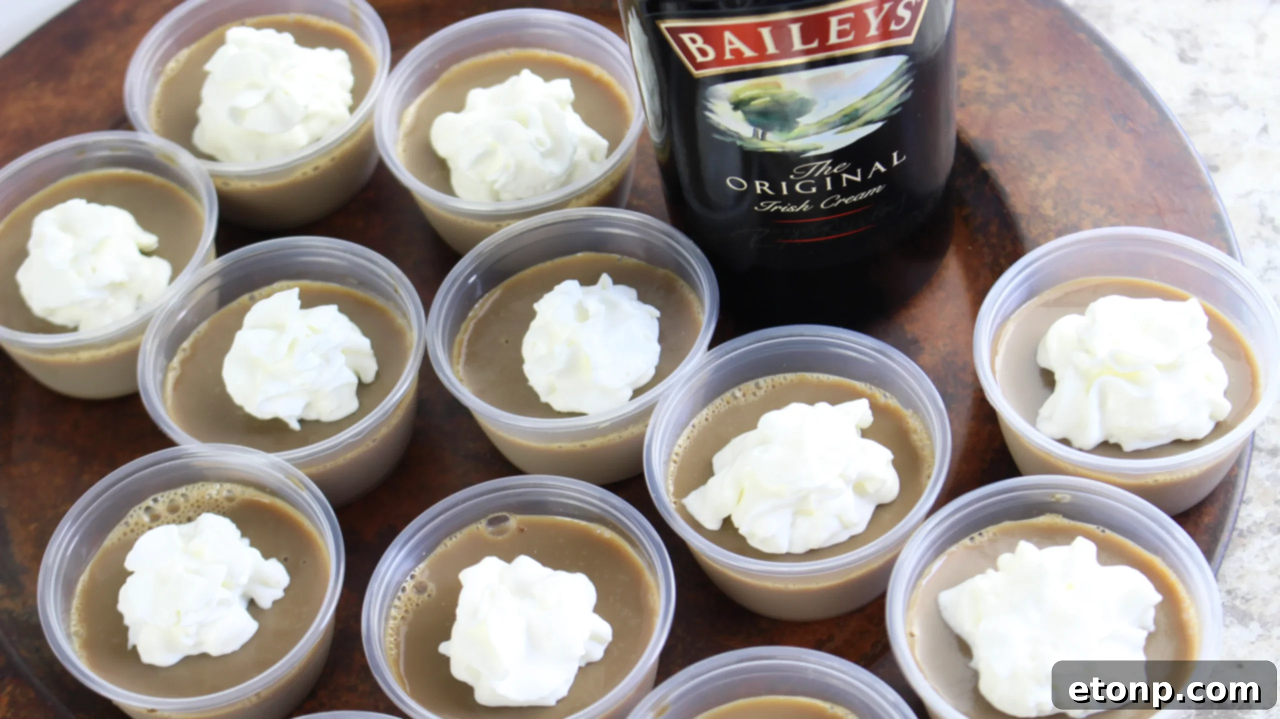Hands preparing Baileys Irish Cream Jello Shots, showing the process of pouring the liquid into cups.