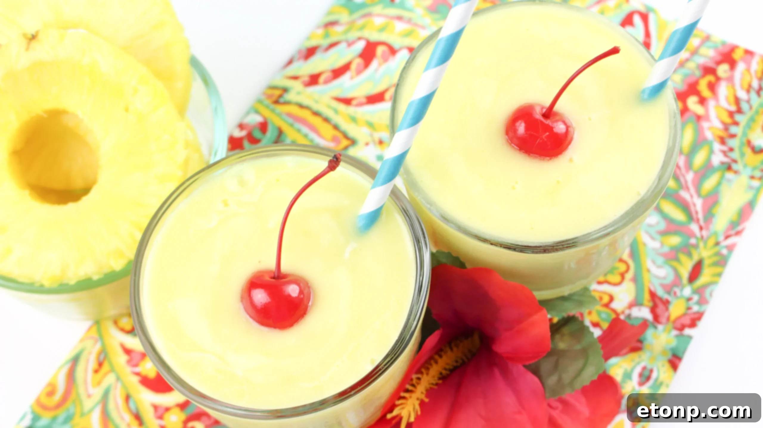 Two perfectly swirled Dole Pineapple Whips, one with a cherry, against a tropical backdrop