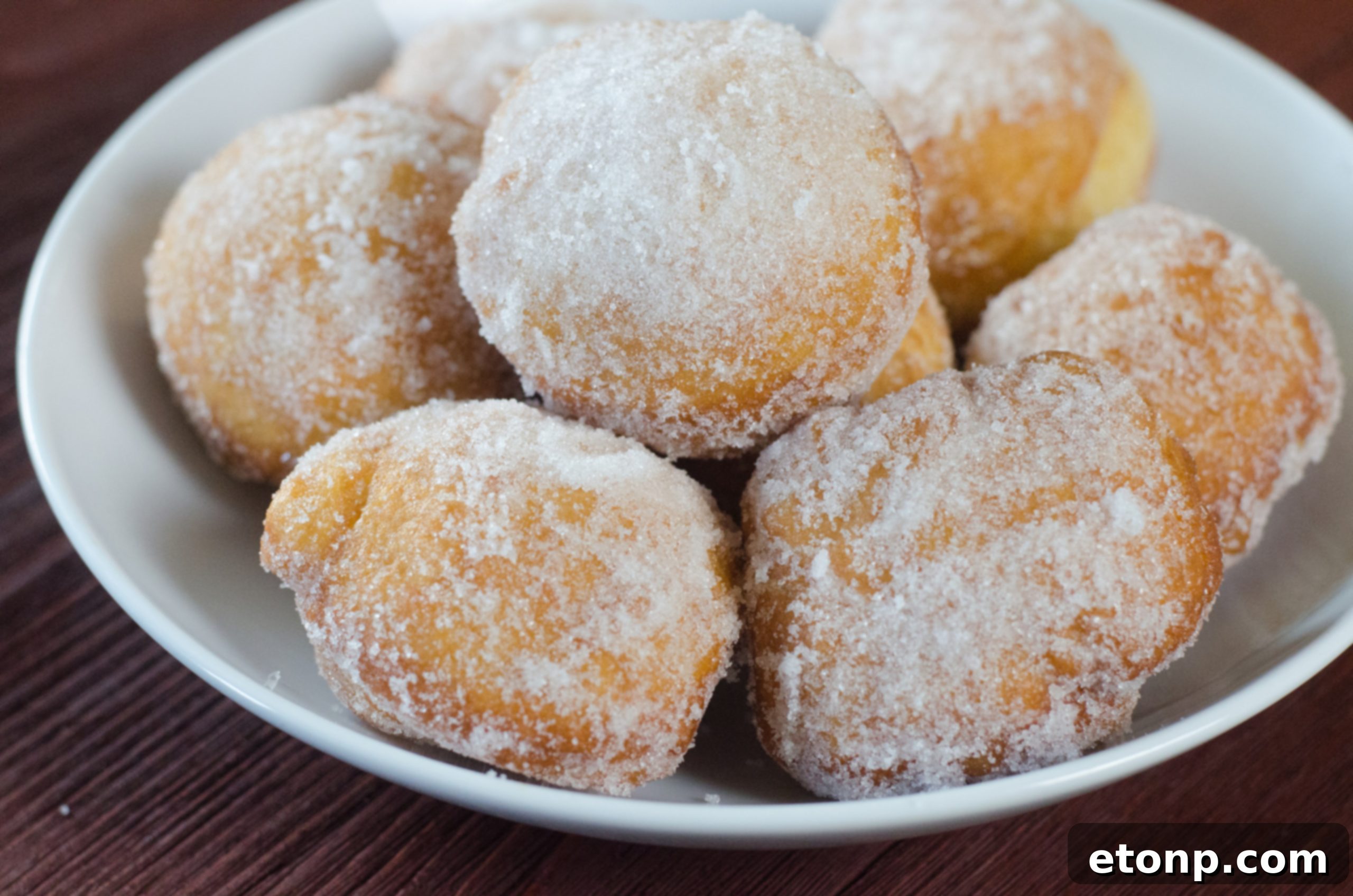A batch of uncooked donut dough balls resting on parchment paper, awaiting their final proof before frying.