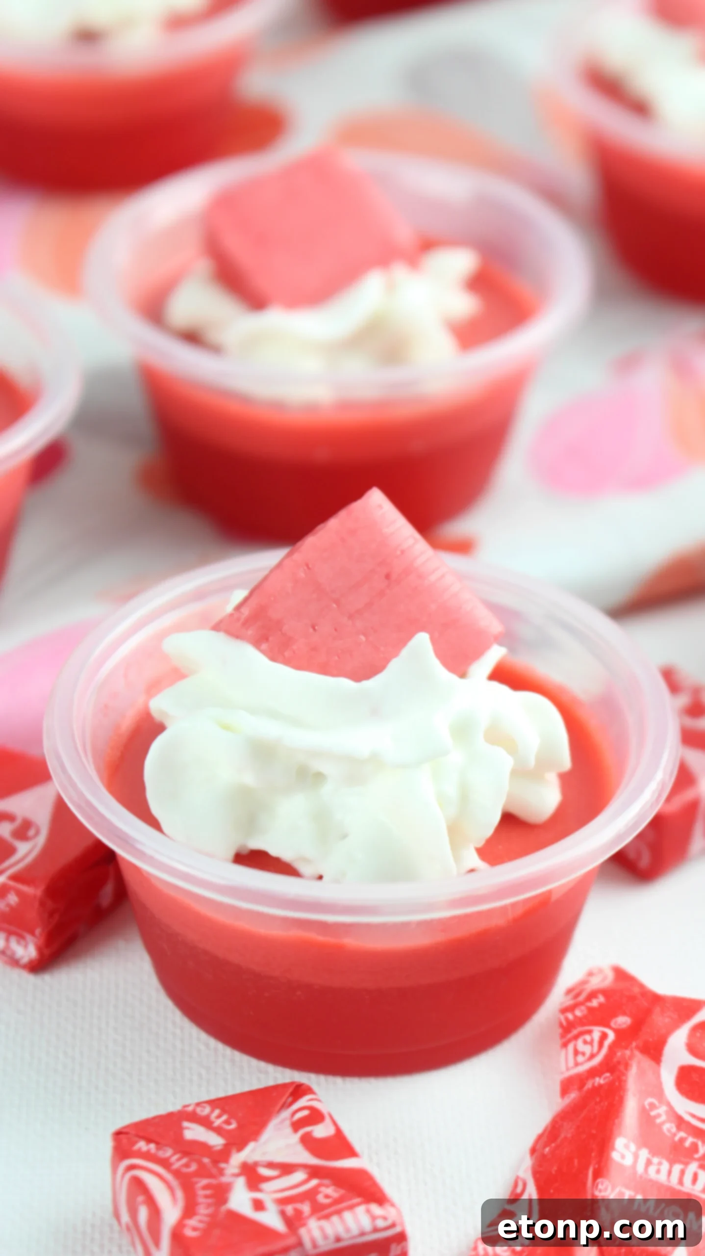 Cherry Starburst Jiggle Pops 2 Close-up of vibrant red Cherry Starburst JELL-O Shots garnished with whipped cream and a cherry Starburst candy, ready for a party.