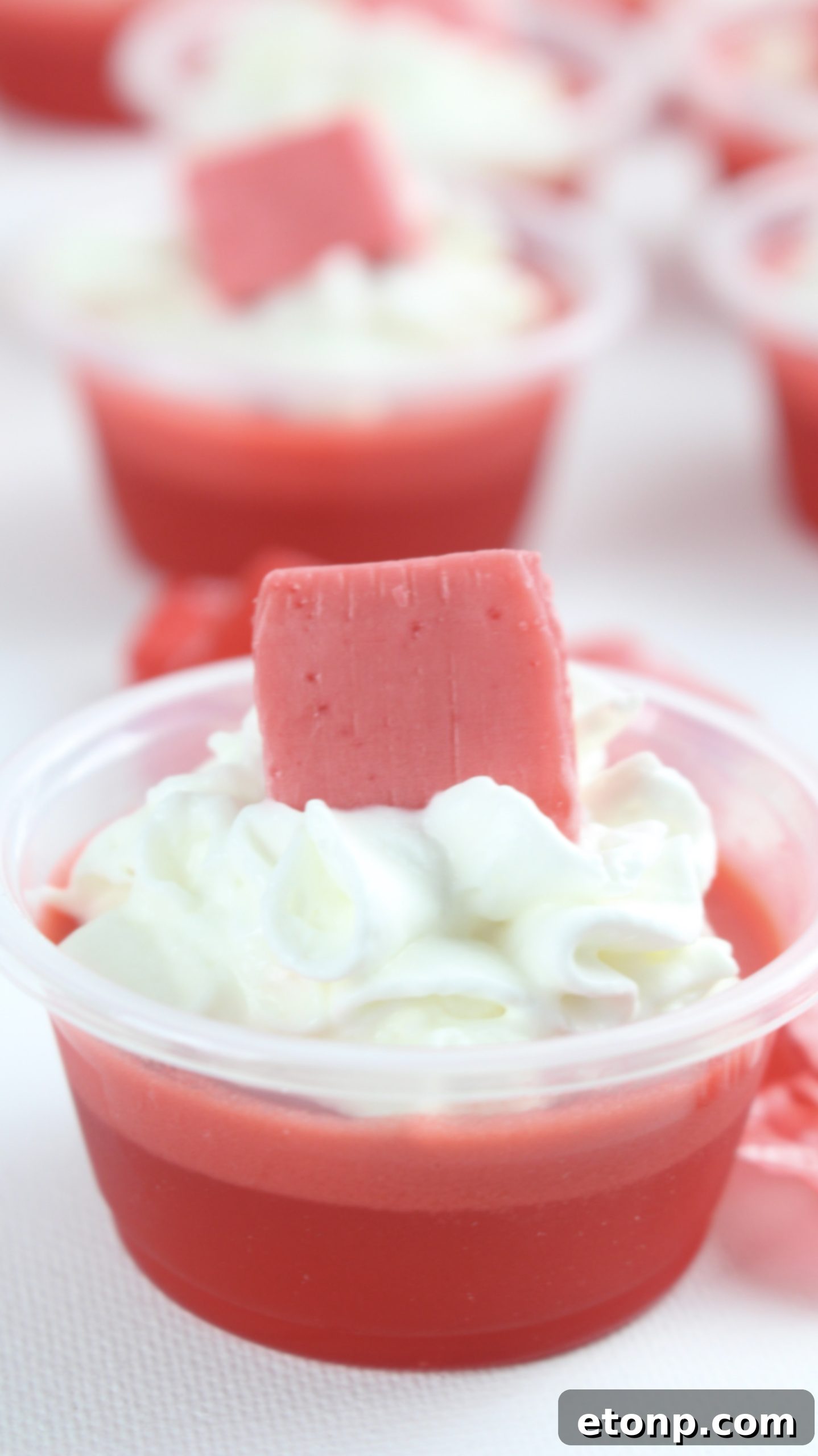 Cherry Starburst Jiggle Pops 10 A close-up of a Cherry Starburst JELL-O Shot, featuring its glossy surface and creamy whipped topping, with a Starburst candy on top.