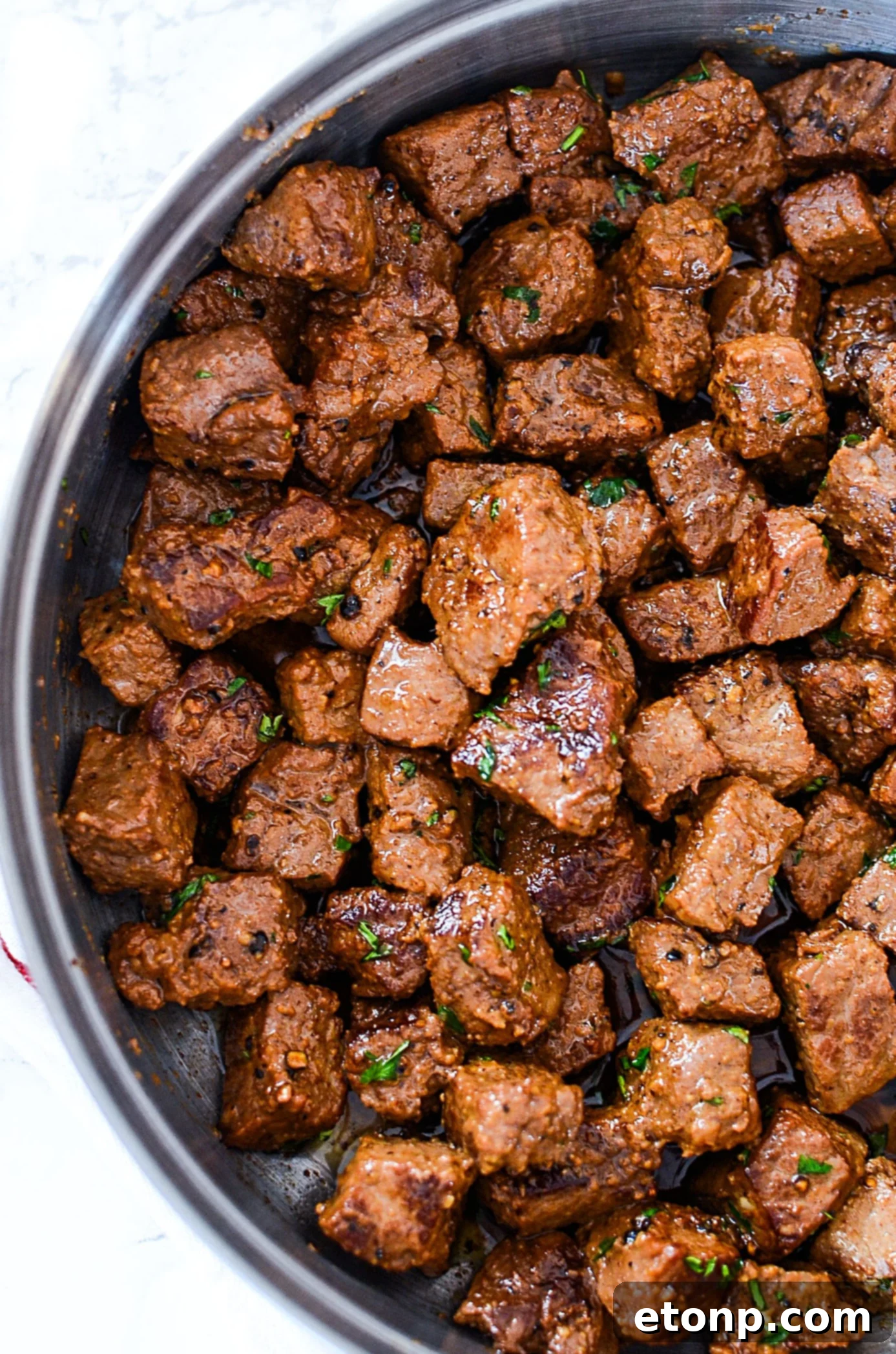 A bowl of garlic butter steak bites, glistening with sauce and topped with fresh parsley.