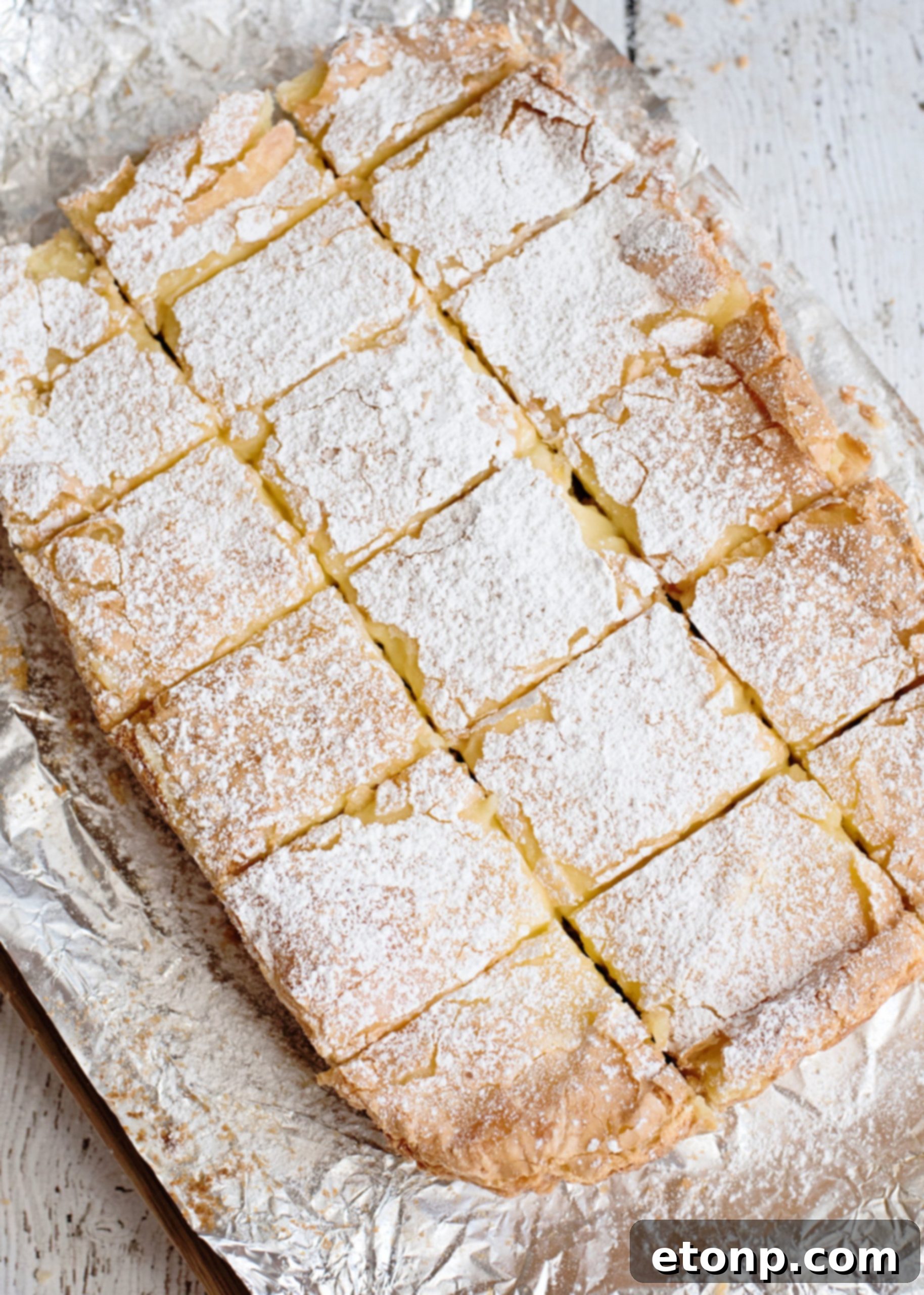 A stack of golden brown Ooey Gooey Butter Bars, dusted with powdered sugar, ready to eat.