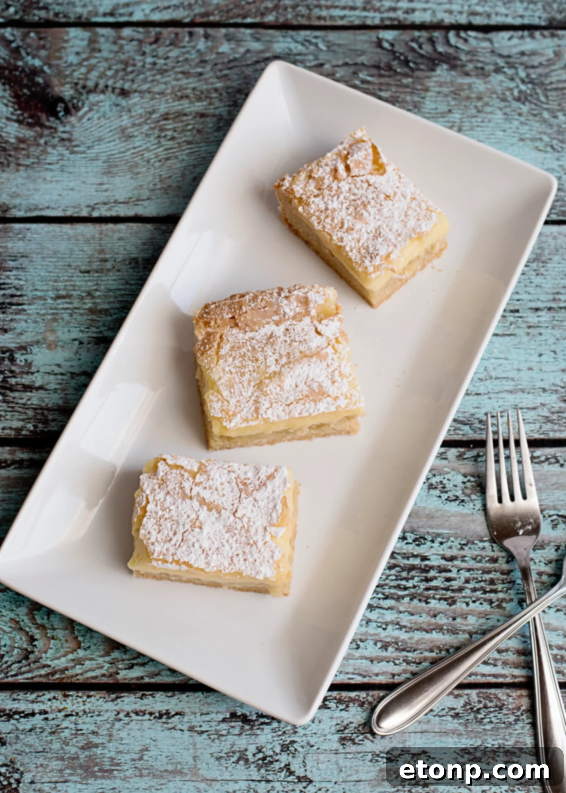 Two Ooey Gooey Butter Bars on a plate, topped with vanilla ice cream and whipped cream.