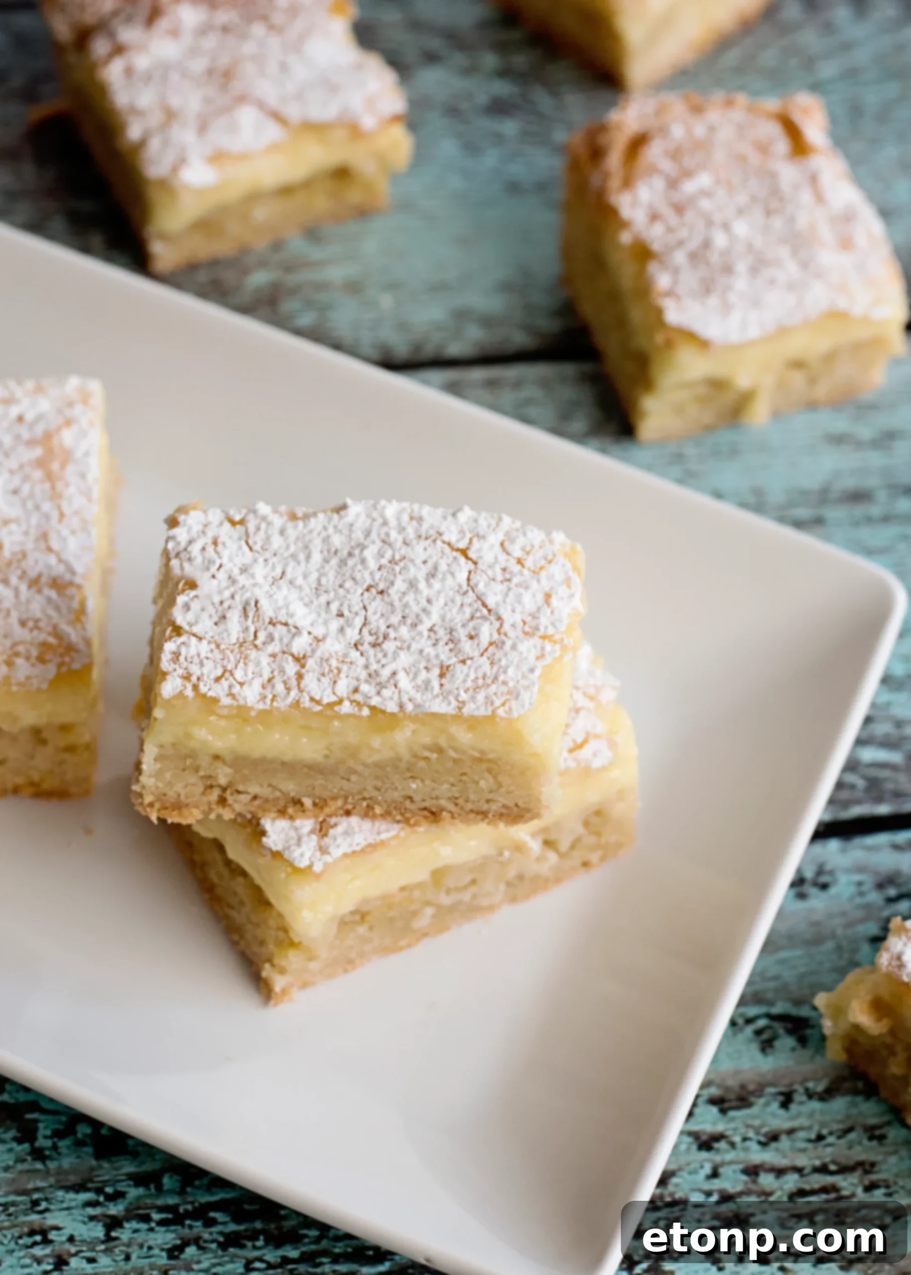 A plate of two perfectly cut Ooey Gooey Butter Bars, dusted with powdered sugar.