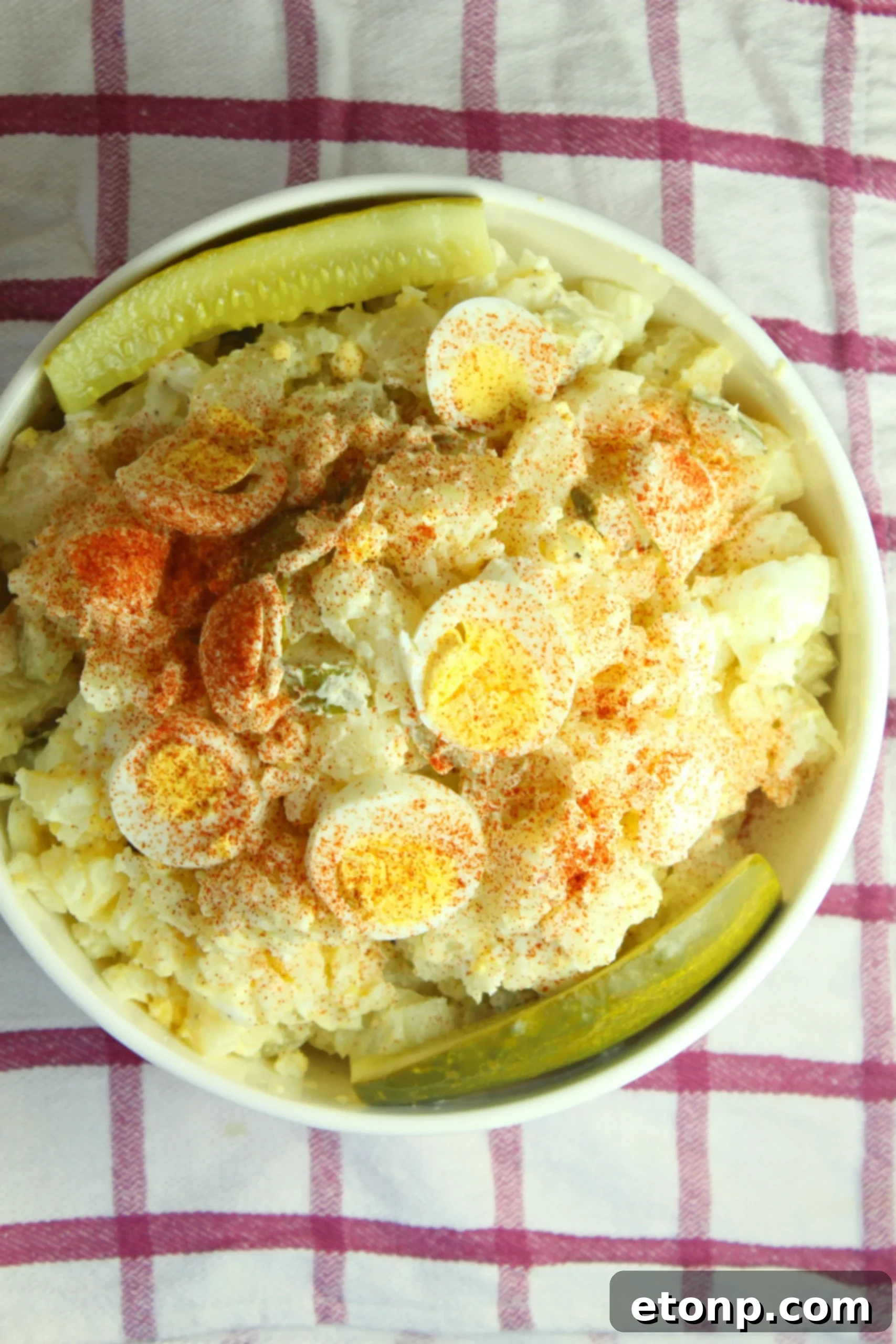 Close-up shot of creamy dill pickle potato egg salad, showcasing the texture and visible pieces of potato, egg, and pickle.