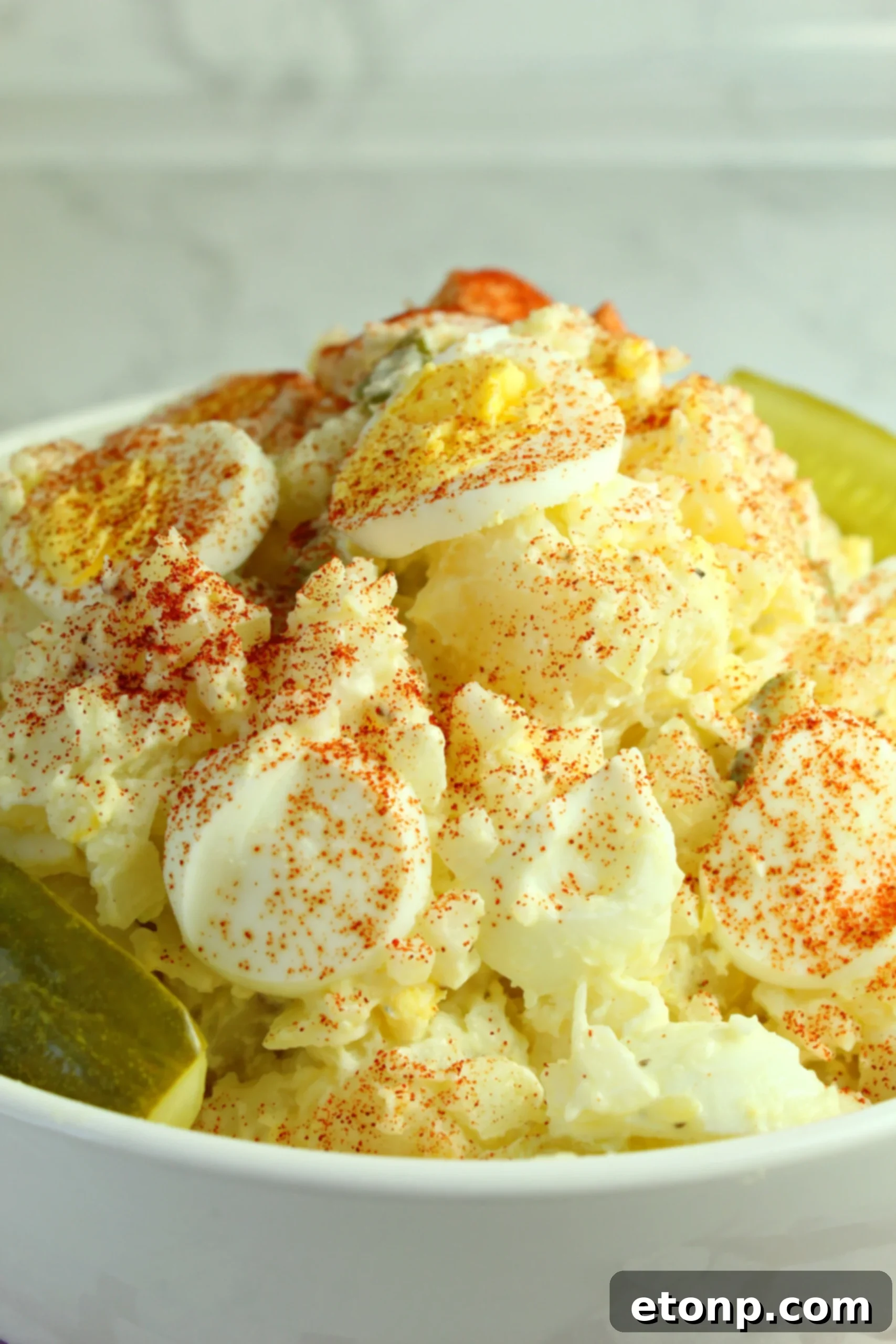 A bowl of fresh dill pickle potato egg salad with a serving spoon, inviting tasters to dig in.