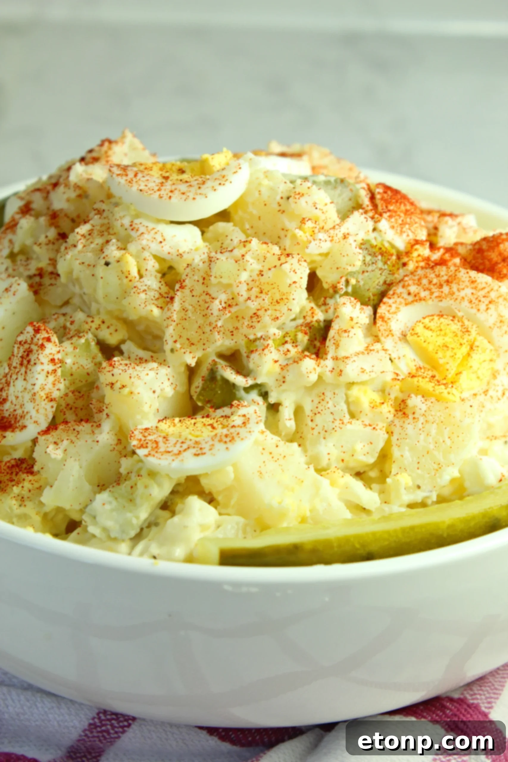 Various ingredients for dill pickle potato egg salad laid out on a table, including potatoes, eggs, pickles, and dressing.