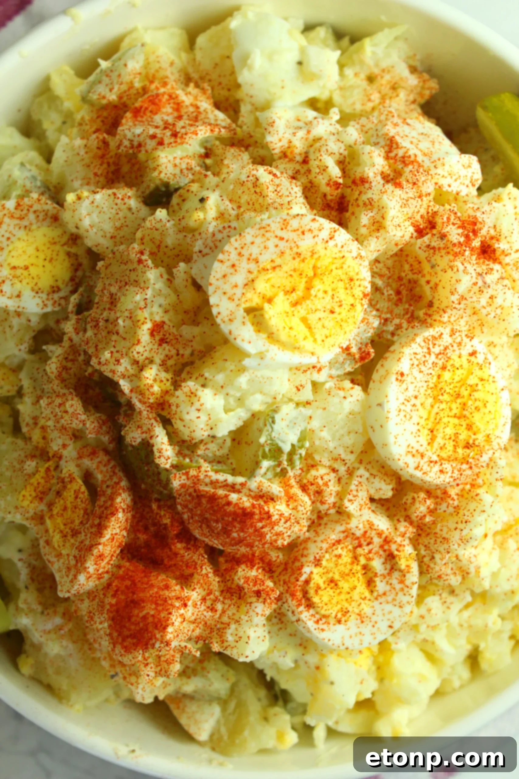 A serving of dill pickle potato egg salad on a plate next to a main dish, emphasizing its role as a perfect side.