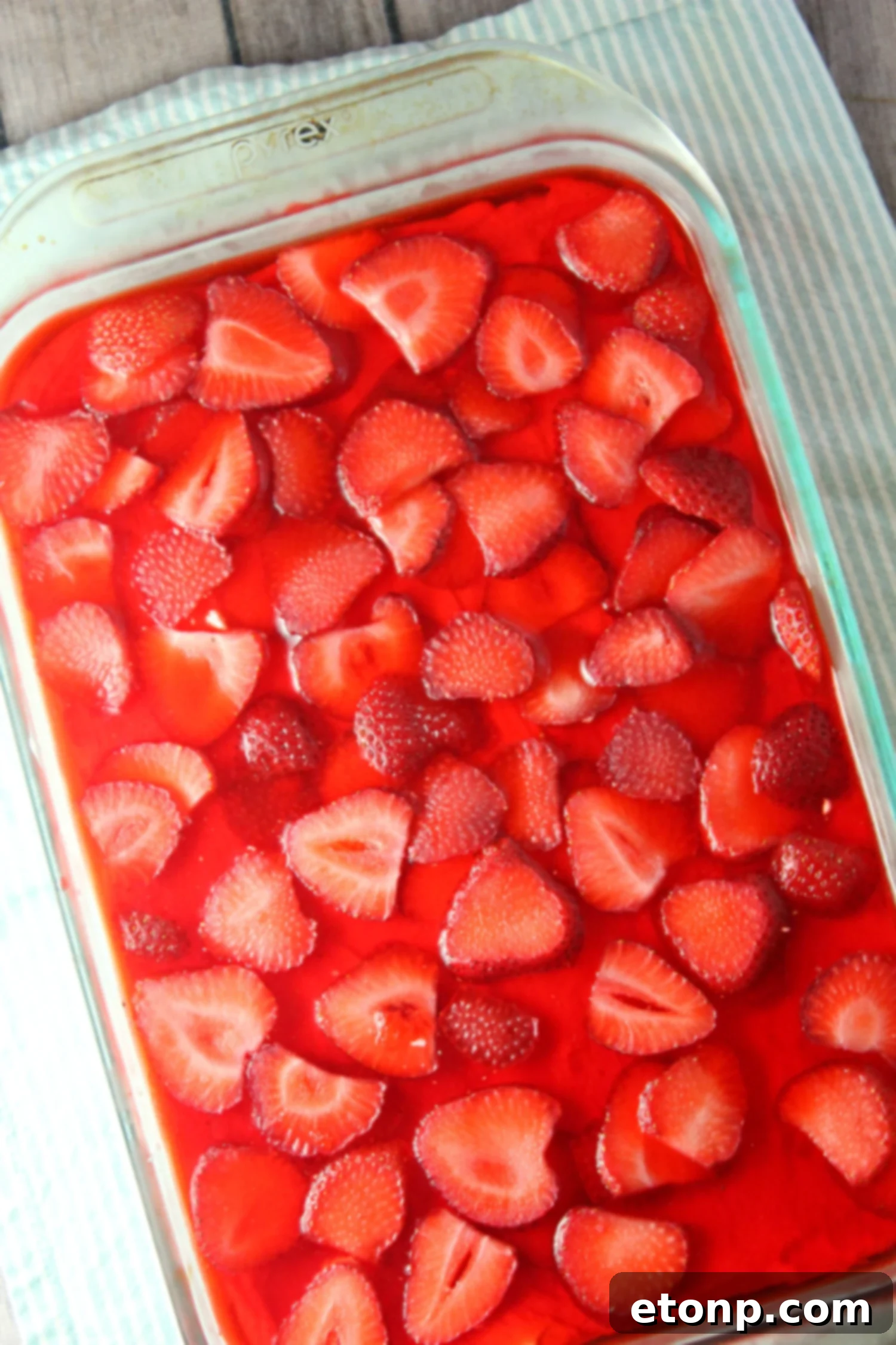 A top-down view of the Strawberry Pretzel Salad in a baking dish, highlighting the vibrant red Jell-O and strawberry pieces.