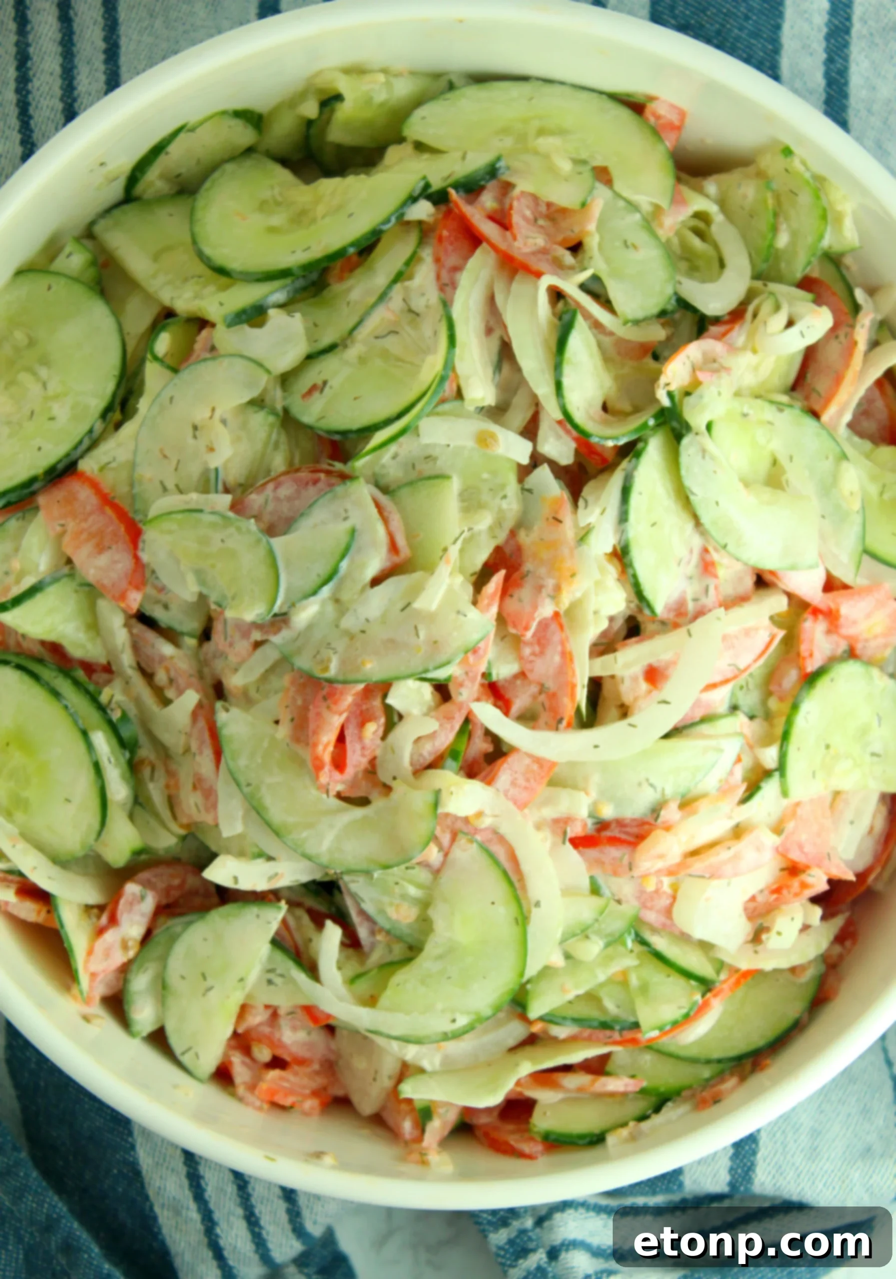 A vibrant, creamy cucumber tomato salad with fresh dill, served in a white bowl, ready to be enjoyed as a refreshing summer dish.