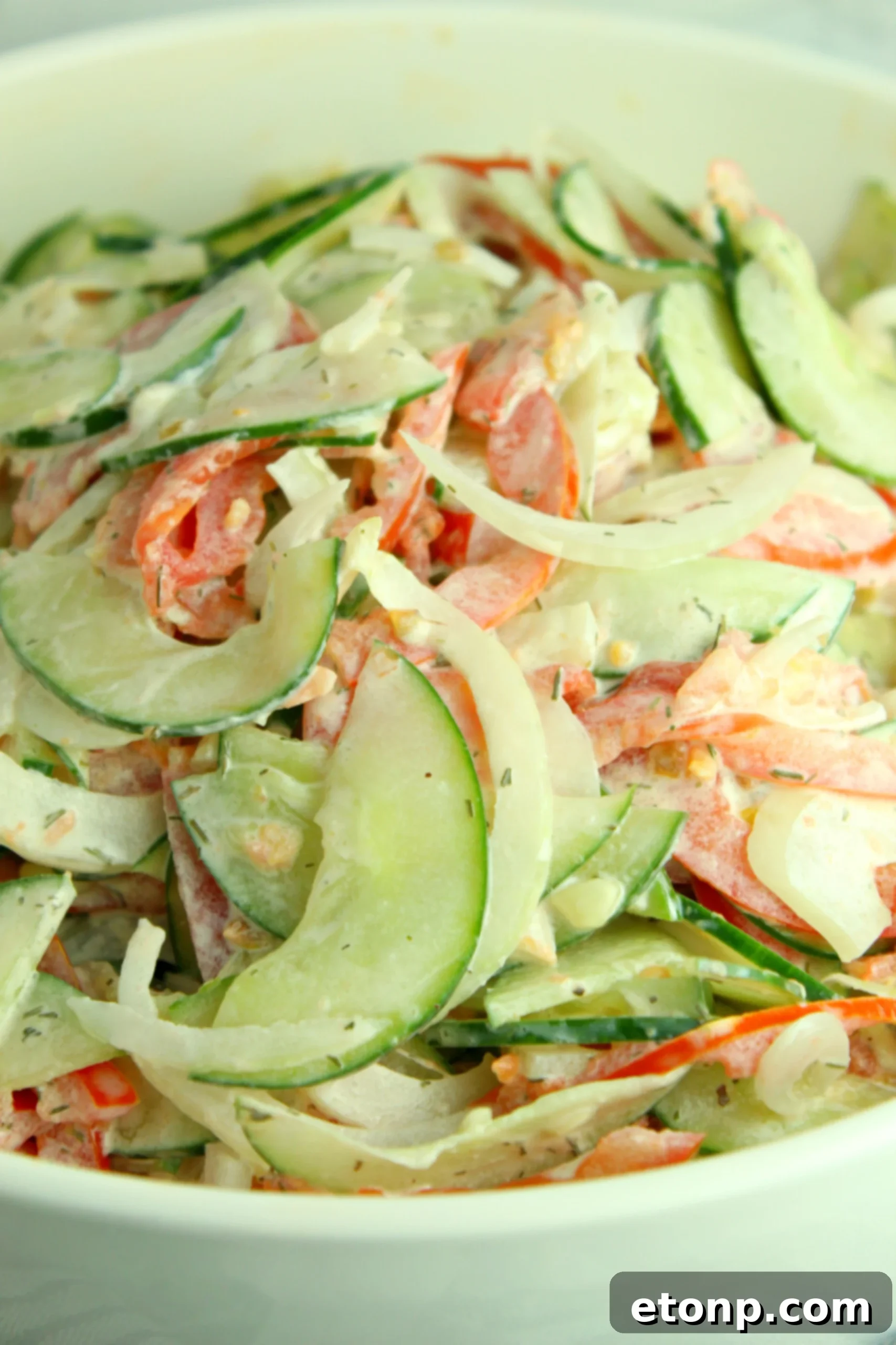 Close-up of creamy cucumber tomato salad with a fork taking a portion, highlighting its fresh ingredients and rich dressing.