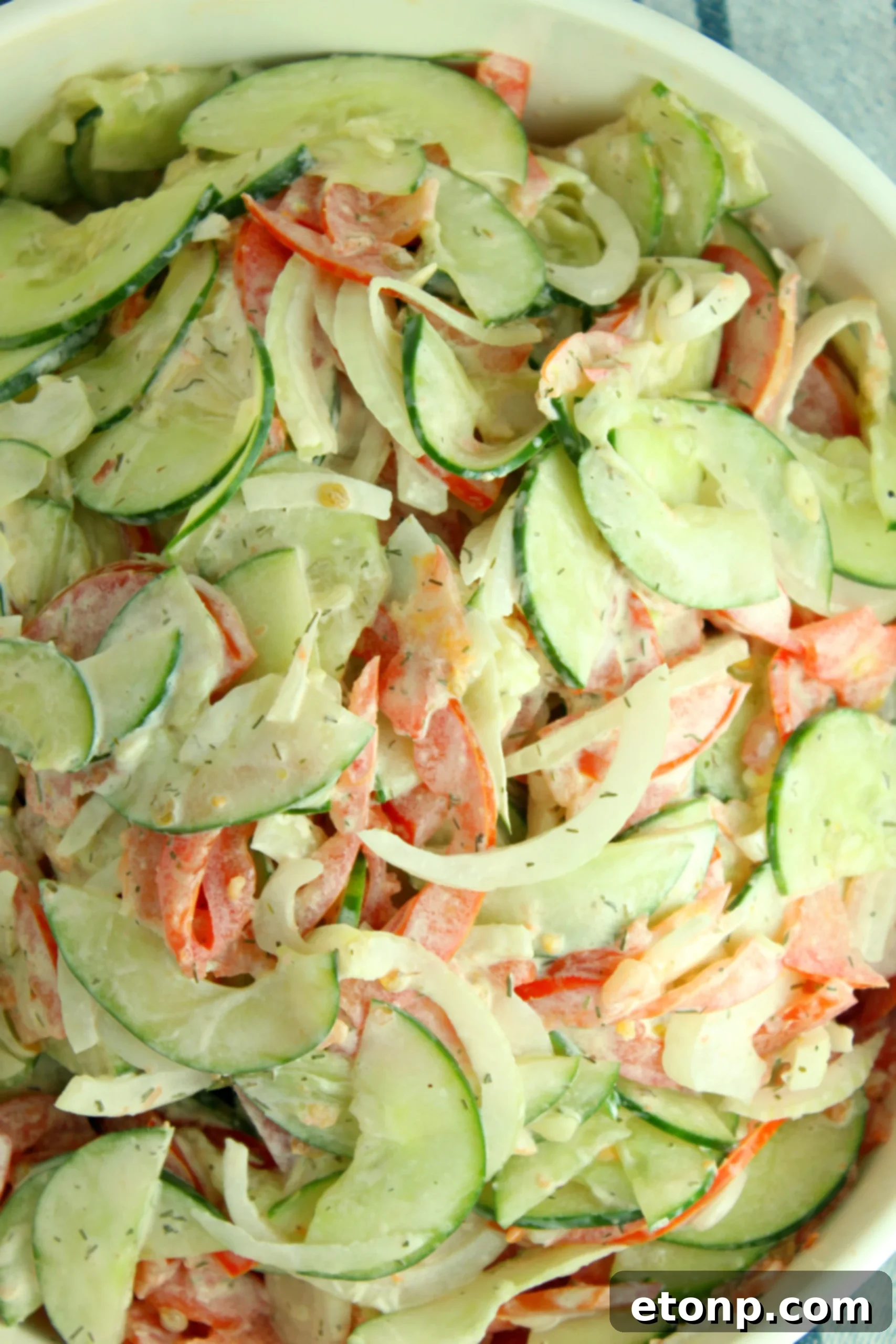 A bowl of creamy cucumber tomato salad, ready to be served at a cookout or pool party, showcasing its vibrant colors.