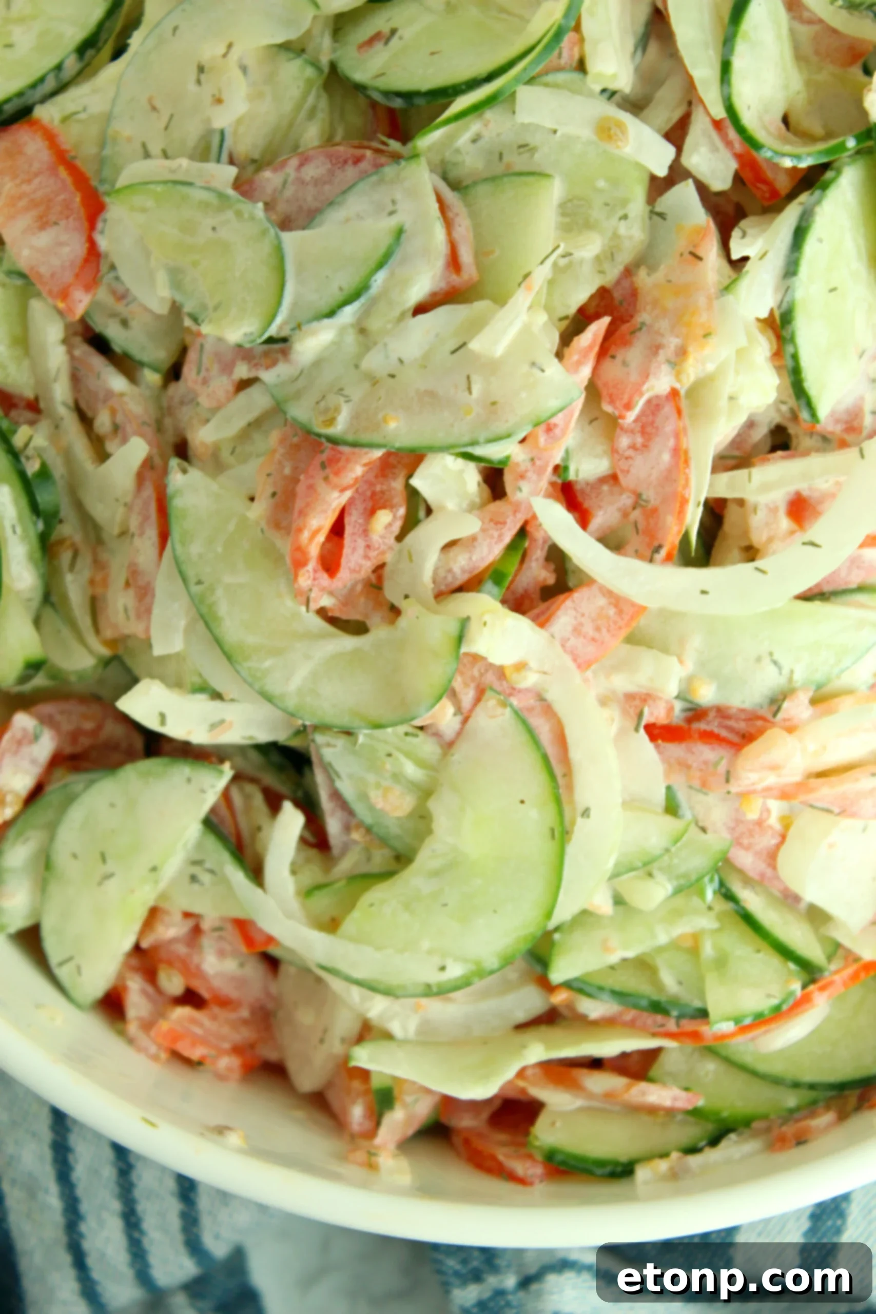 A close-up of thinly sliced sweet onions and Roma tomatoes, ready to be mixed into the creamy dressing.