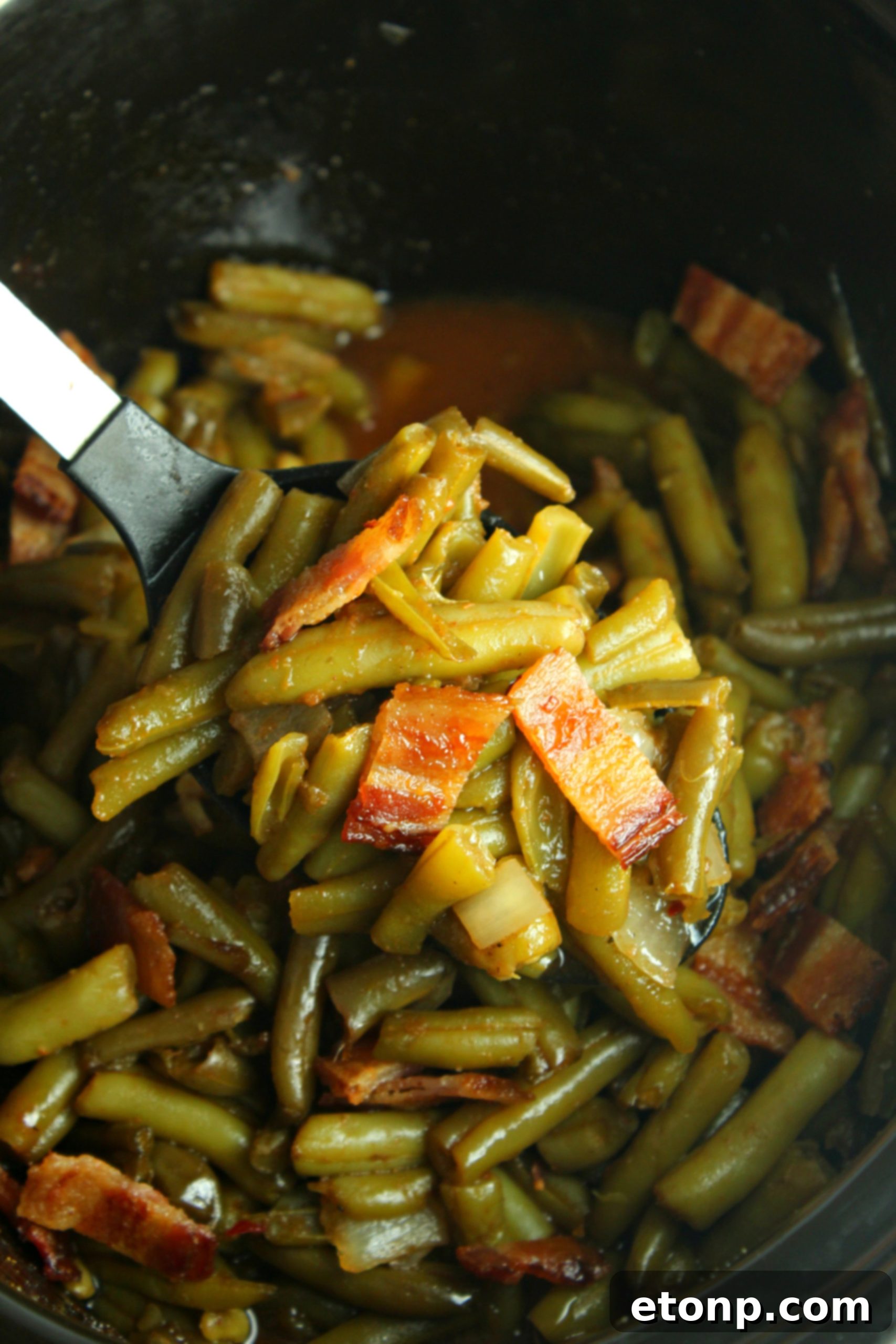 The slow cooker filled with green beans, onions, and bacon, ready for cooking