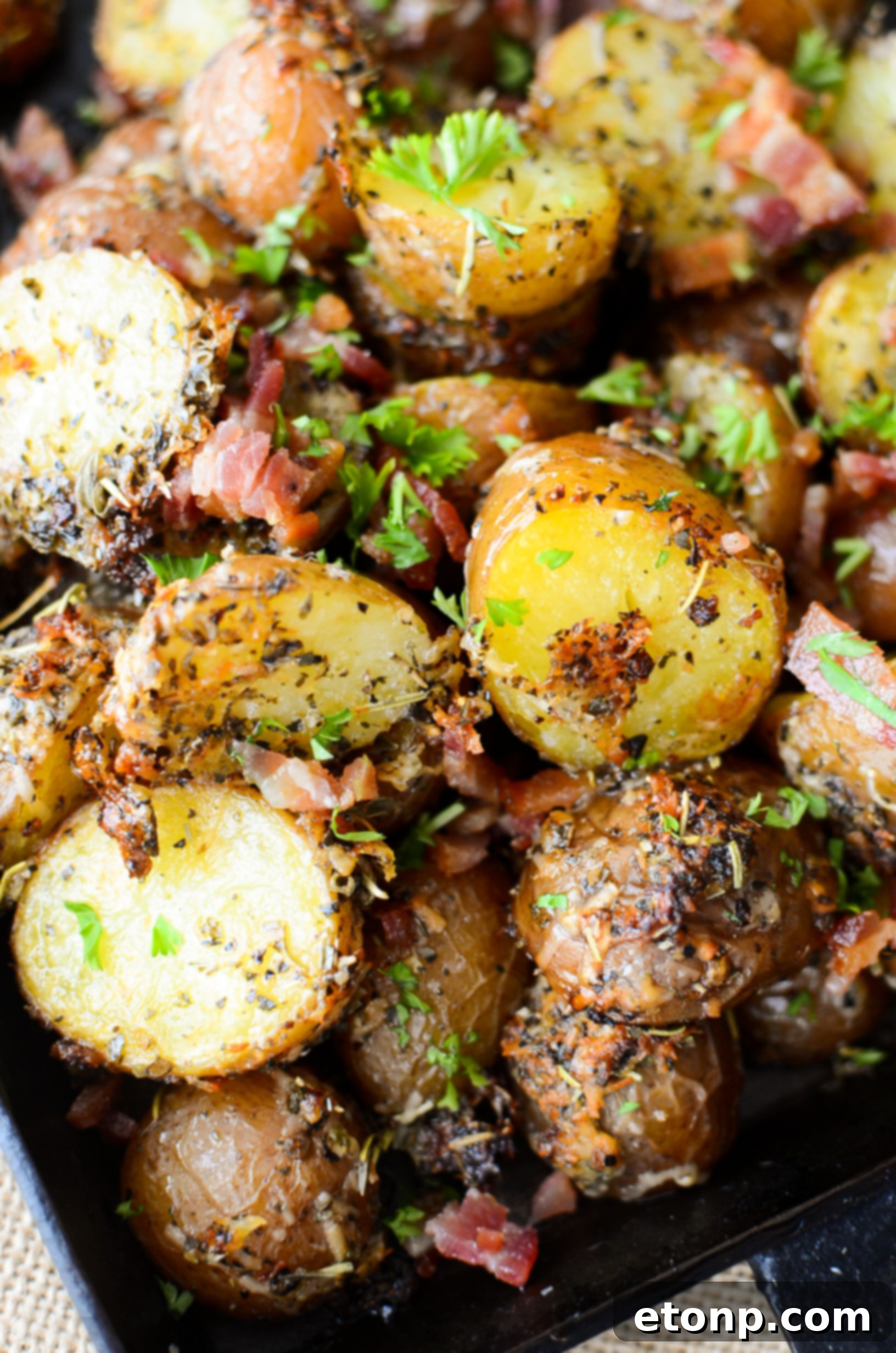 Close-up of golden brown Parmesan Crusted Roasted Potatoes with crispy bacon bits, served in a rustic dish.