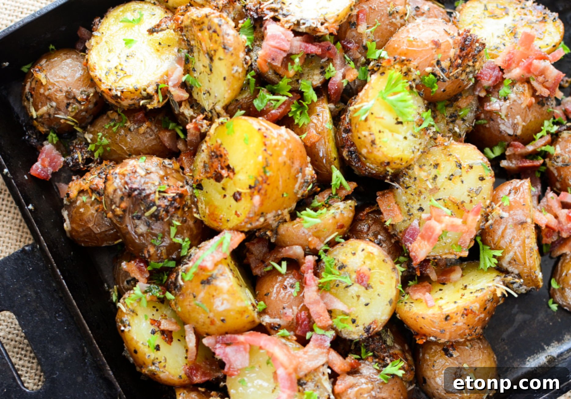 Bowl of uncooked baby potatoes, halved and ready for roasting, next to a selection of fresh spices.
